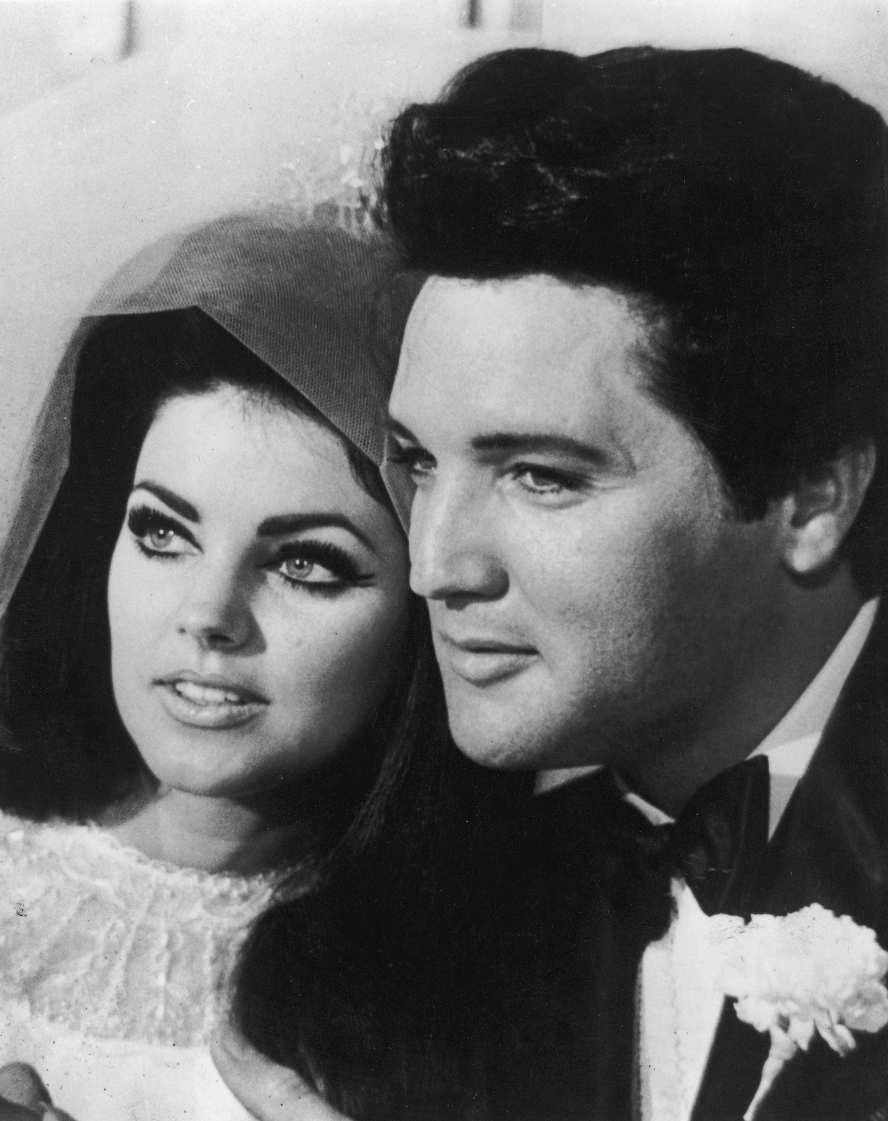 Priscilla Beaulieu poses closely beside her new husband, Elvis Presley, following their wedding ceremony in Las Vegas on May 1, 1967, featuring her dramatic bouffant styled with a veil and beaded bridal lace alongside Elvis in a classic black tuxedo, bow tie, and white floral boutonnière.