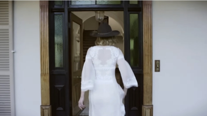 The dark wooden double doors open to reveal a glimpse inside the farmhouse, where rich timber trim and a grand staircase hint at the timeless interior beyond. From a video dated July 20, 2015. | Source: YouTube/Vogue