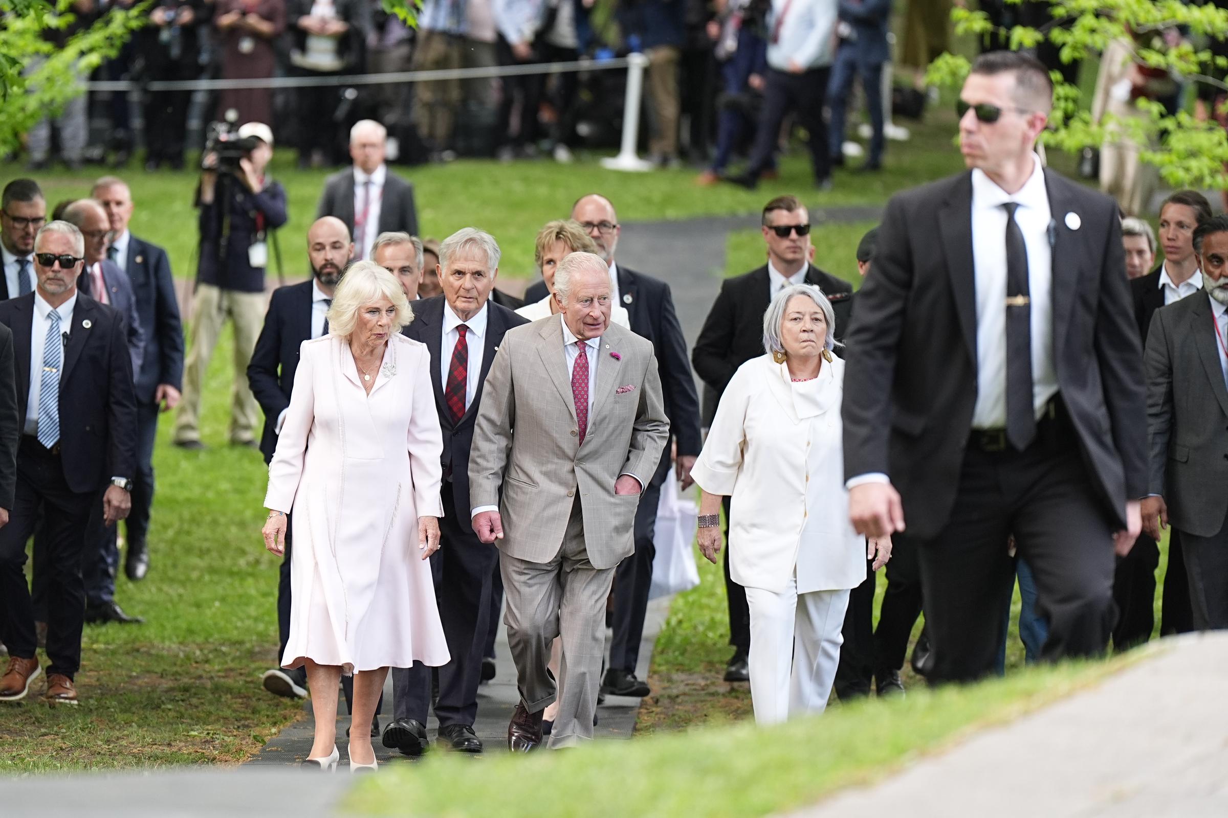 King Charles III and Queen Camilla depart the tree planting ceremony near the site of the sugar maple they planted during their 2017 tour of Canada, accompanied by security personnel and officials.