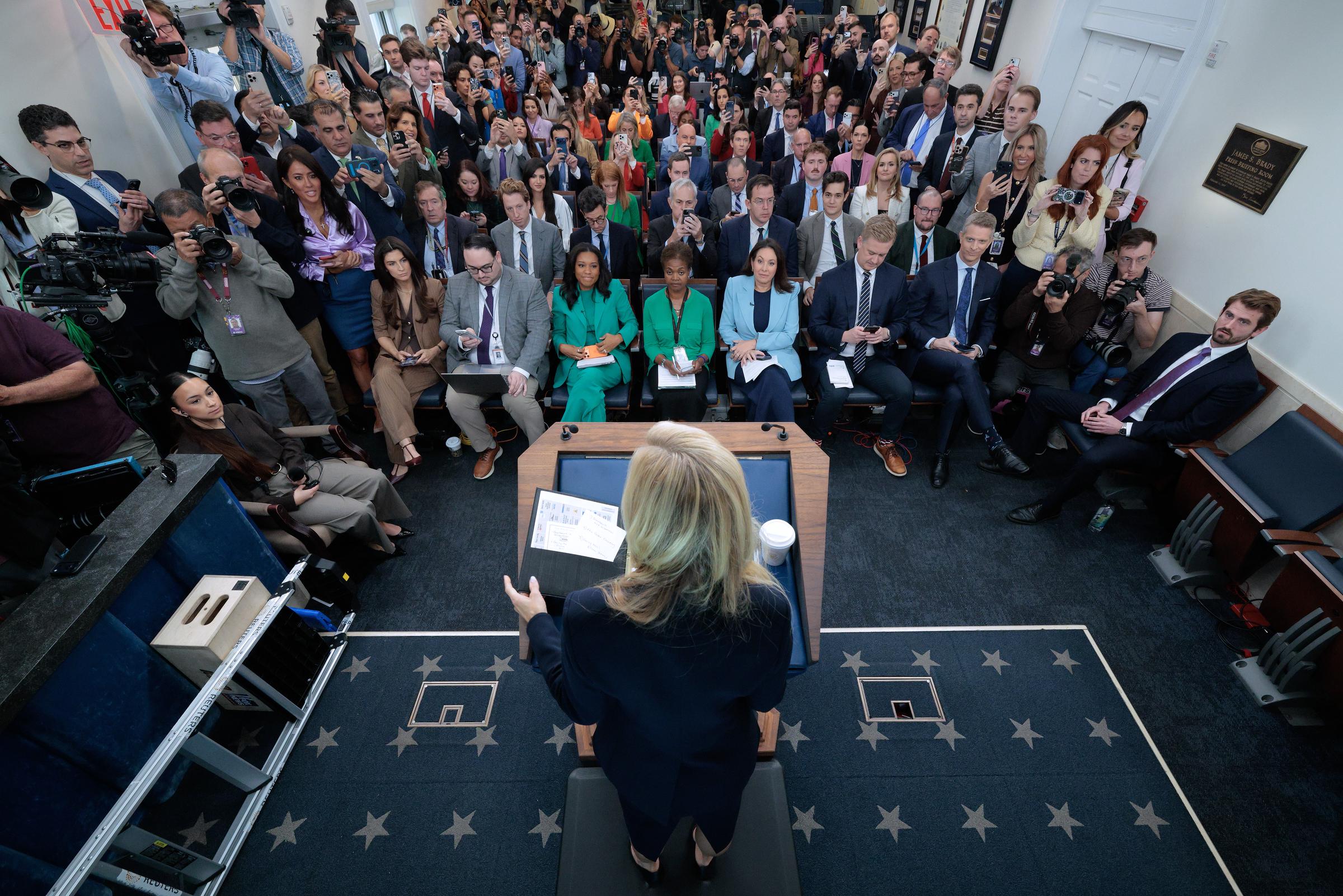 Katie Zacharia addresses a packed White House briefing room during her first appearance as press secretary, with reporters gathered around the podium as she delivers her opening remarks. | Source: Getty Images