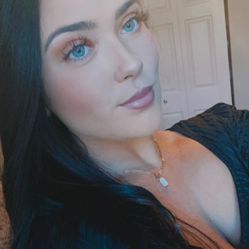 Hannah Jorgensen poses for a soft indoor selfie wearing a dark scoop-neck top, a delicate pendant necklace, and featuring dark brunette hair. | Source: Facebook/Hannah Jorgensen