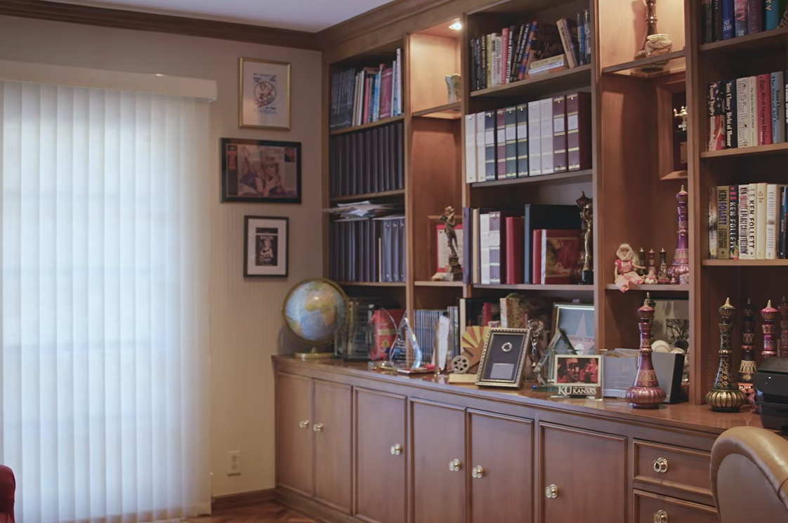 A look inside Barbara Eden's home office reveals floor-to-ceiling wooden shelves filled with books, neatly arranged binders, framed photographs, awards, and colorful genie-themed collectibles. | Source: YouTube/People
