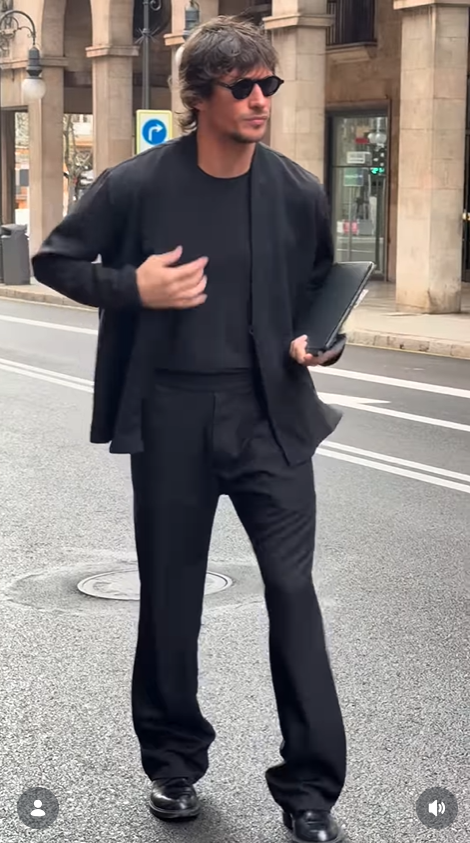 Jake Hall walks through a city street dressed in an all-black outfit while carrying a laptop. | Source: Instagram/jakehall