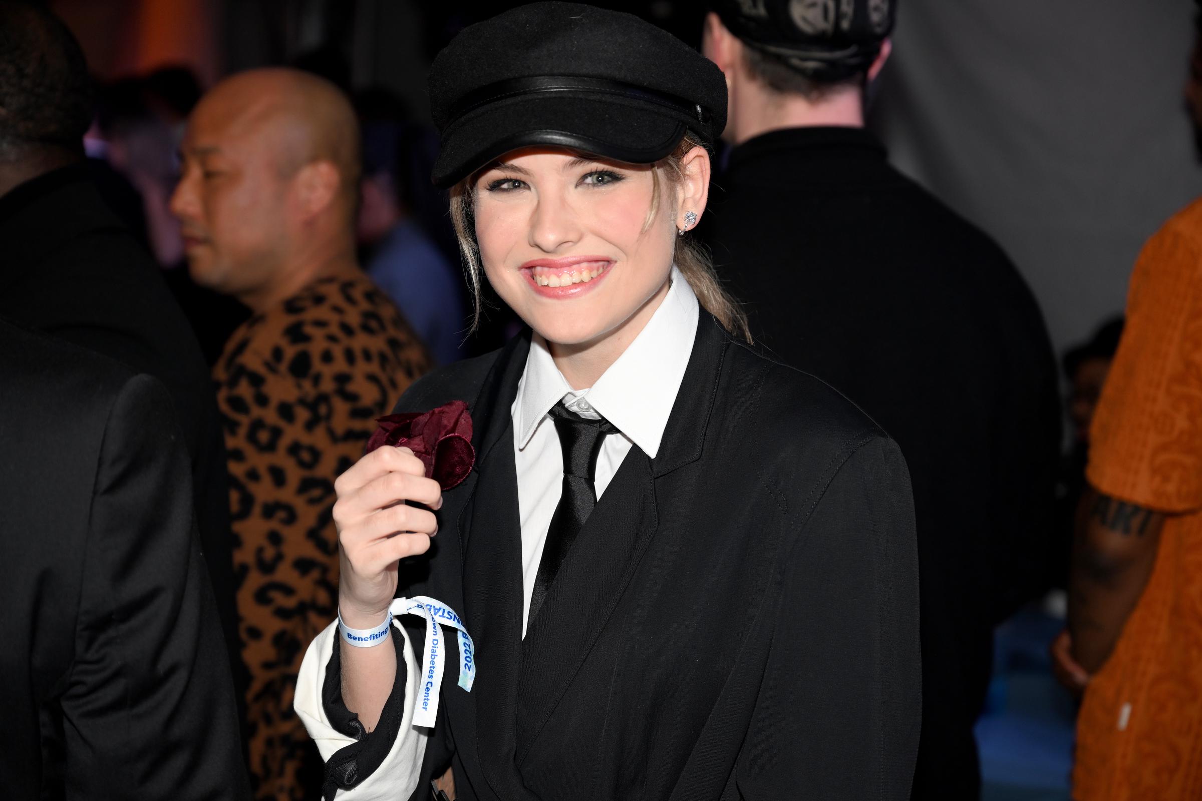 Departing entirely from the soft pastels and voluminous floral hats of her earlier Derby appearances, 15-year-old Dannielynn Birkhead showcased a bold and striking stylistic pivot at the Barnstable Brown Gala on May 6, 2022. Ensembled in a sharp menswear-inspired black suit, a crisp white button-down shirt, a dark necktie, and a chic black newsboy cap, she flashed a wide, radiant smile that underscored a dramatic transformation and a fearless embrace of a sharper, more sophisticated edge.