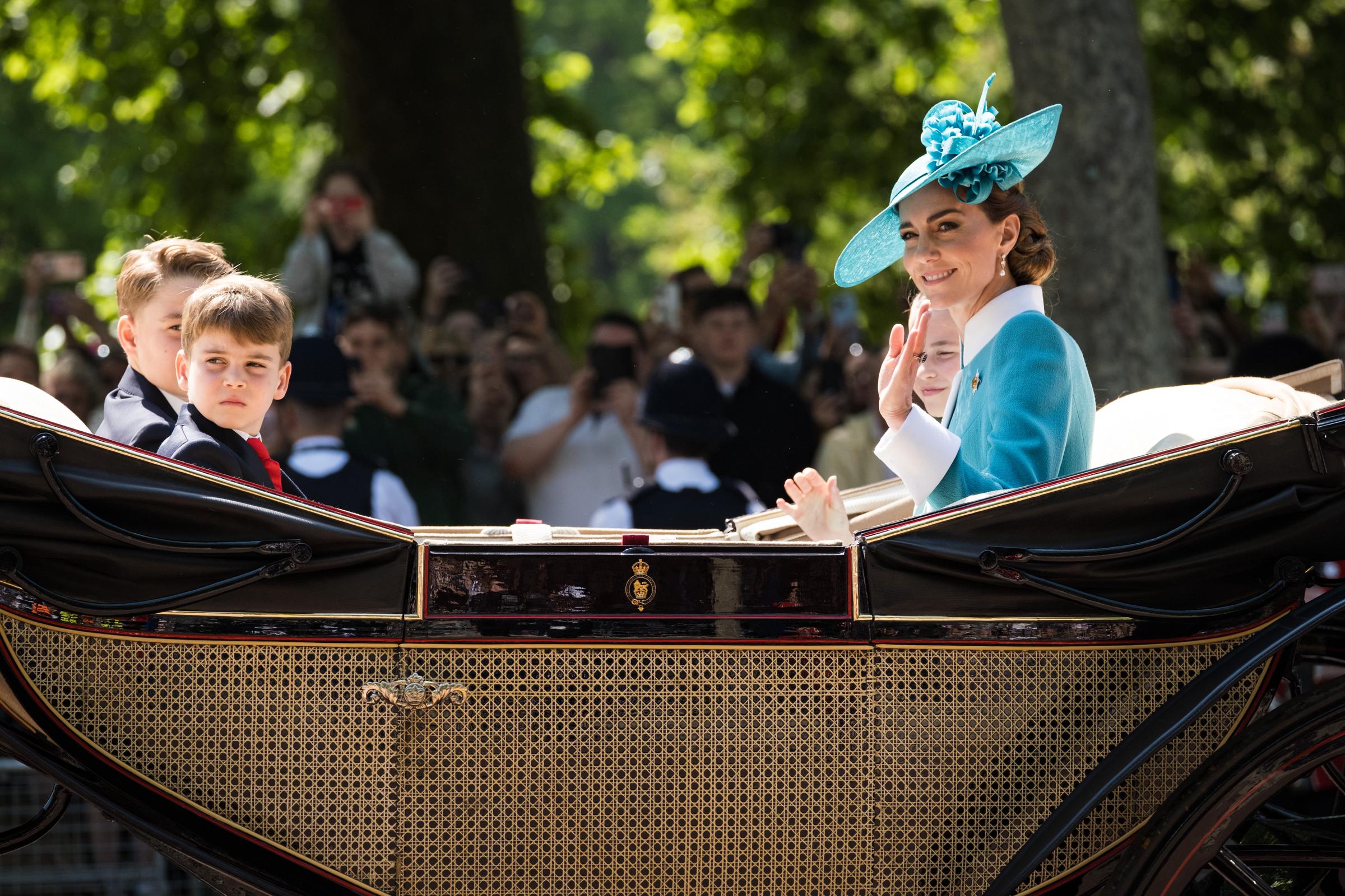 Princess Charlotte, Princess Catherine, Prince George, and Prince Louis ride in the royal carriage as Catherine and Princess Charlotte wave to the people.