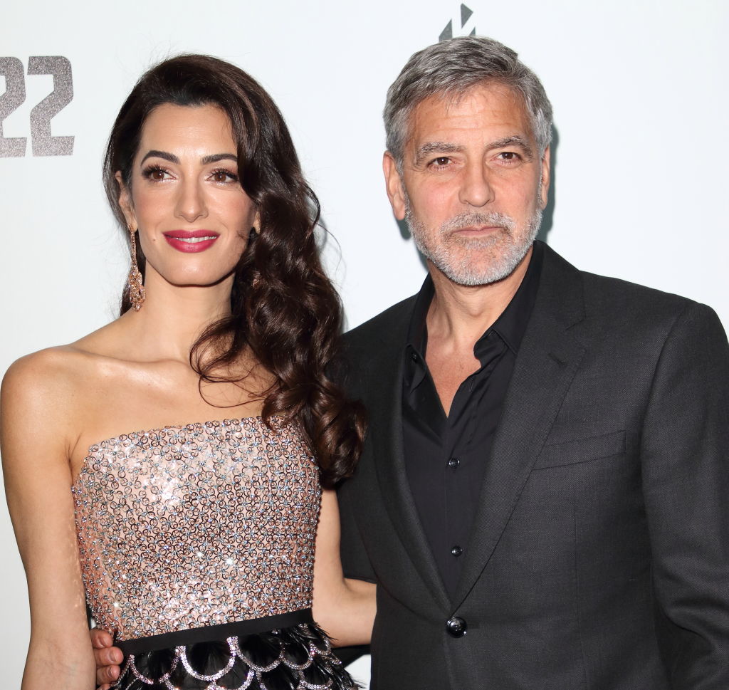George Clooney poses alongside his wife, Amal Clooney, at a public event in an older photo. Amal wears a strapless, embellished gown with a black waistband and dangling earrings, while George sports a dark suit over a black shirt. | Source: Getty Images