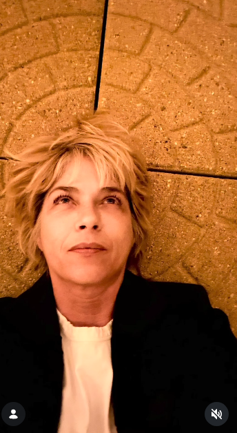 Selma Blair reclines against an ornate arched stone surface, gazing thoughtfully toward the ceiling on October 11, 2026. Soft lighting falls across her blonde hair and casual black tailored jacket worn over a simple white tee. | Source: Instagram/selmablair