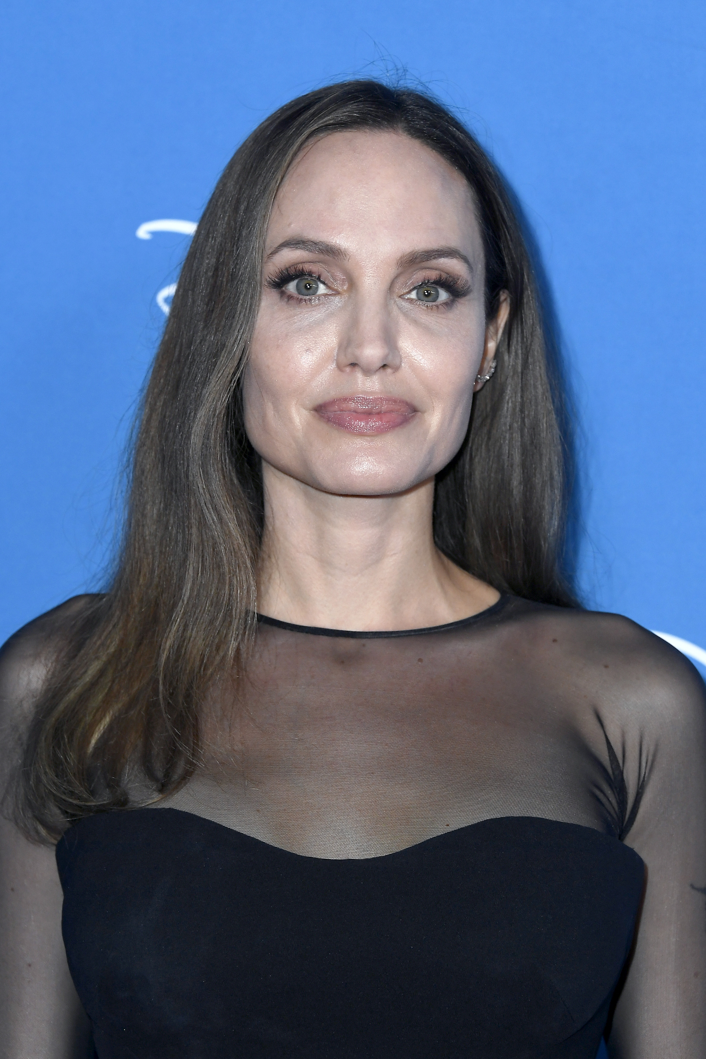 At the D23 Expo, Jolie wore her hair in a sleek, straight style with a center part. The long, medium brown strands were left loose with minimal layering, giving the look a clean, understated appearance with a smooth, natural texture.