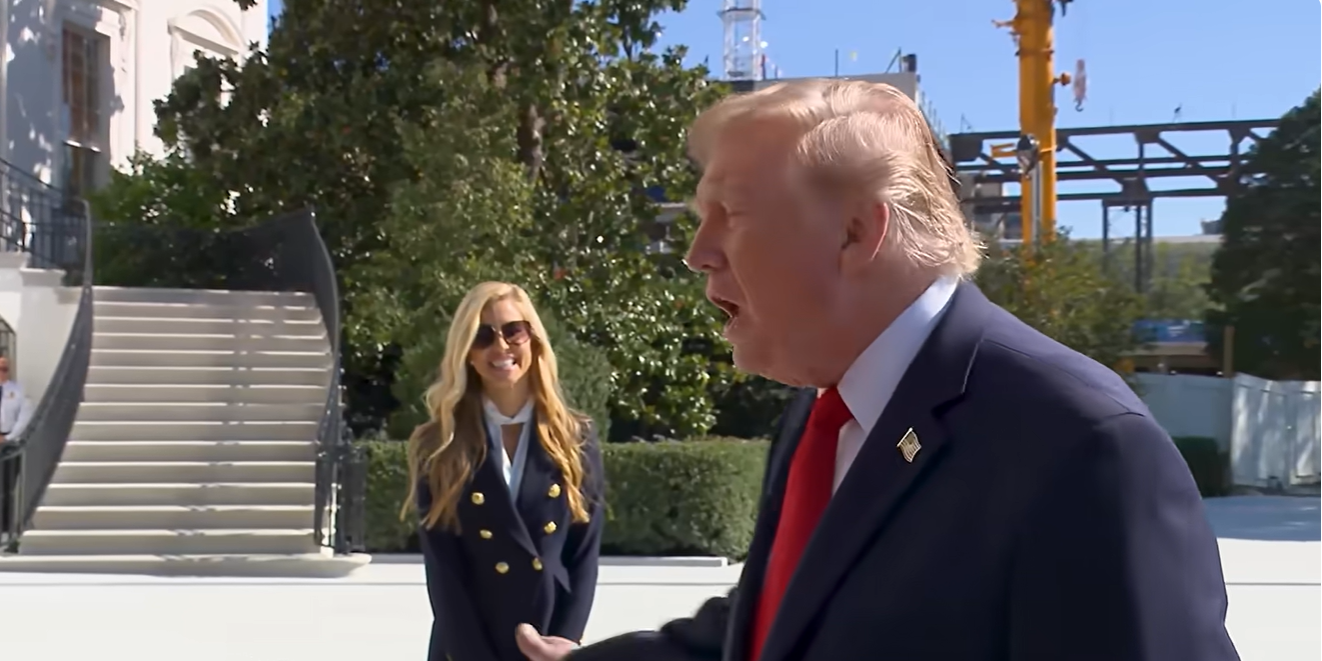 Donald Trump answers reporters' questions outside the White House as Katie Zacharia stands behind him following her first press briefing, during which he praised her performance. | Source: YouTube/New York Post