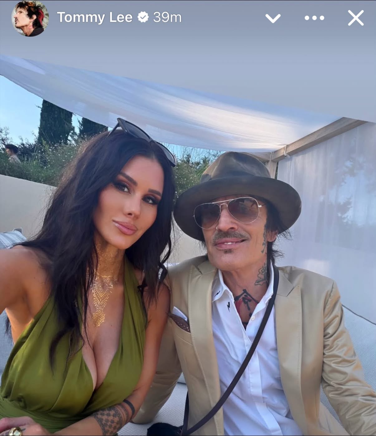 Brittany Furlan posed beside Tommy Lee in his Instagram Story, wearing a plunging olive-green halter dress that closely matched the color of Pamela’s flowing fringed look. | Source: Instagram/tommylee