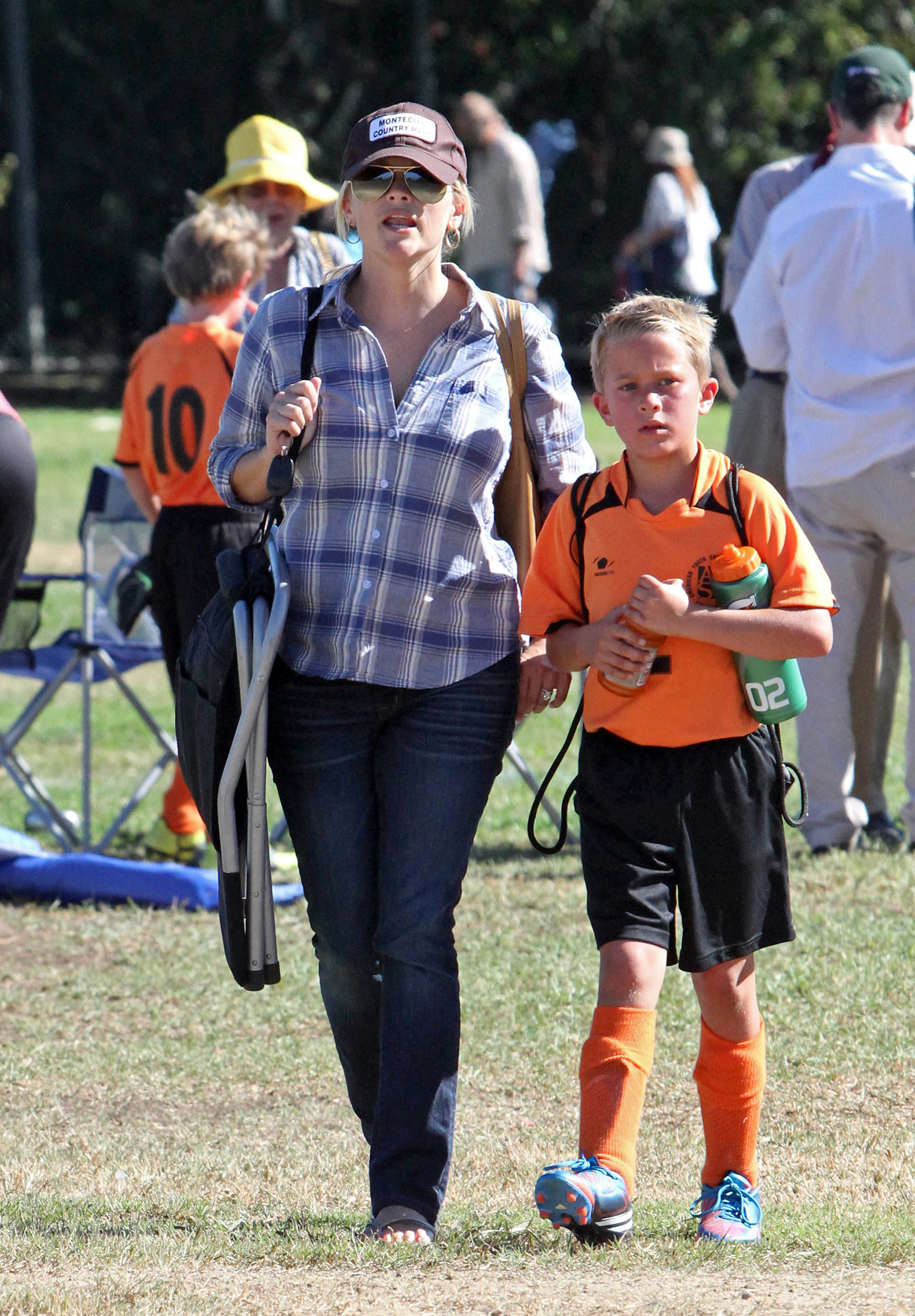 Reese Witherspoon walks with Deacon Phillippe in Los Angeles, dressed casually in a plaid shirt and jeans as he wears a bright orange soccer uniform. | Source: Getty Images