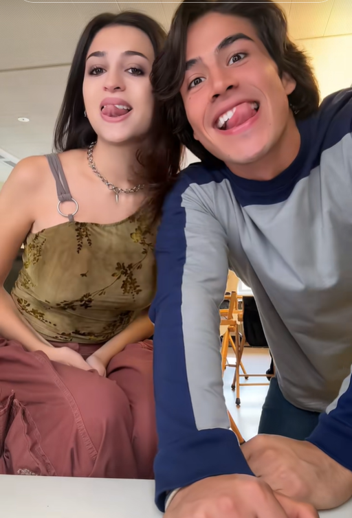 Josie Totah and her male companion make playful faces at the camera in another moment from the TikTok video. Josie wears the same olive-green floral top and pink trousers, accessorized with a silver chain necklace and a shoulder strap. | Source: TikTok/josie totah