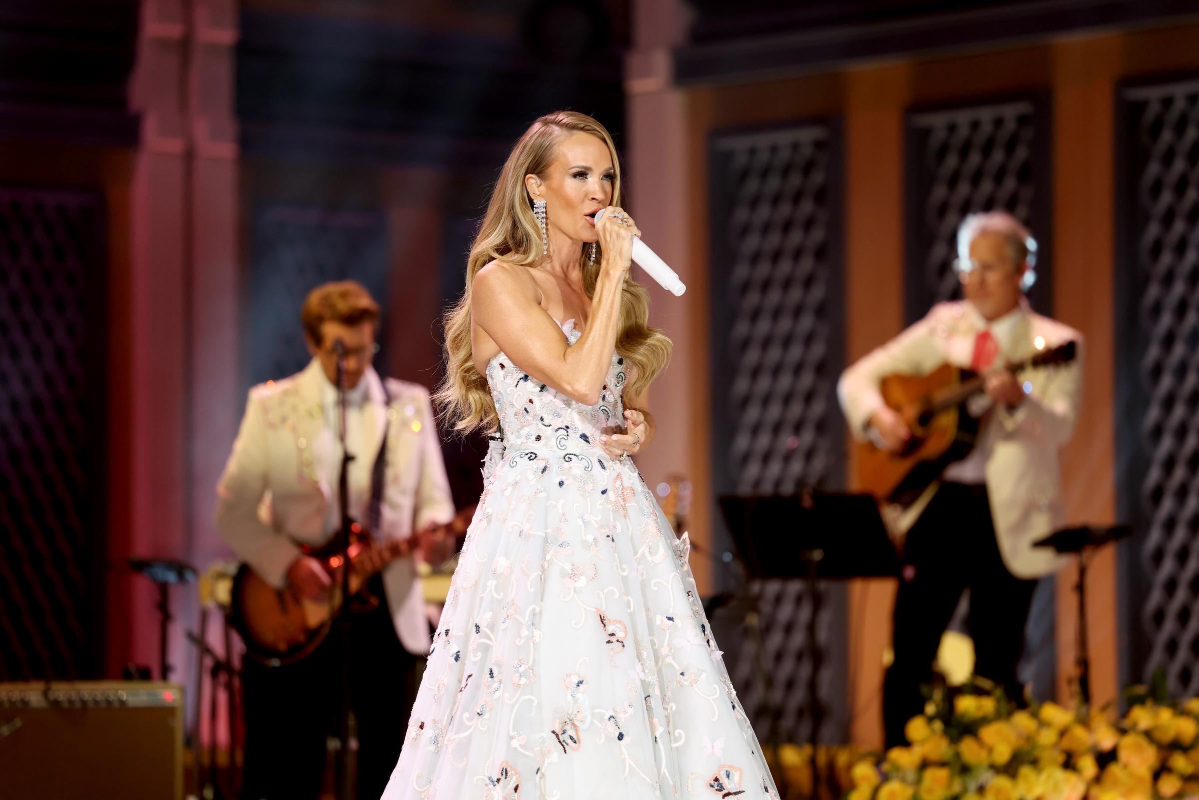 Carrie Underwood performs alongside musicians dressed in white jackets during the Dolly Parton tribute, wearing a butterfly-embroidered gown as part of the evening's tribute to the country legend. | Source: Getty Images.