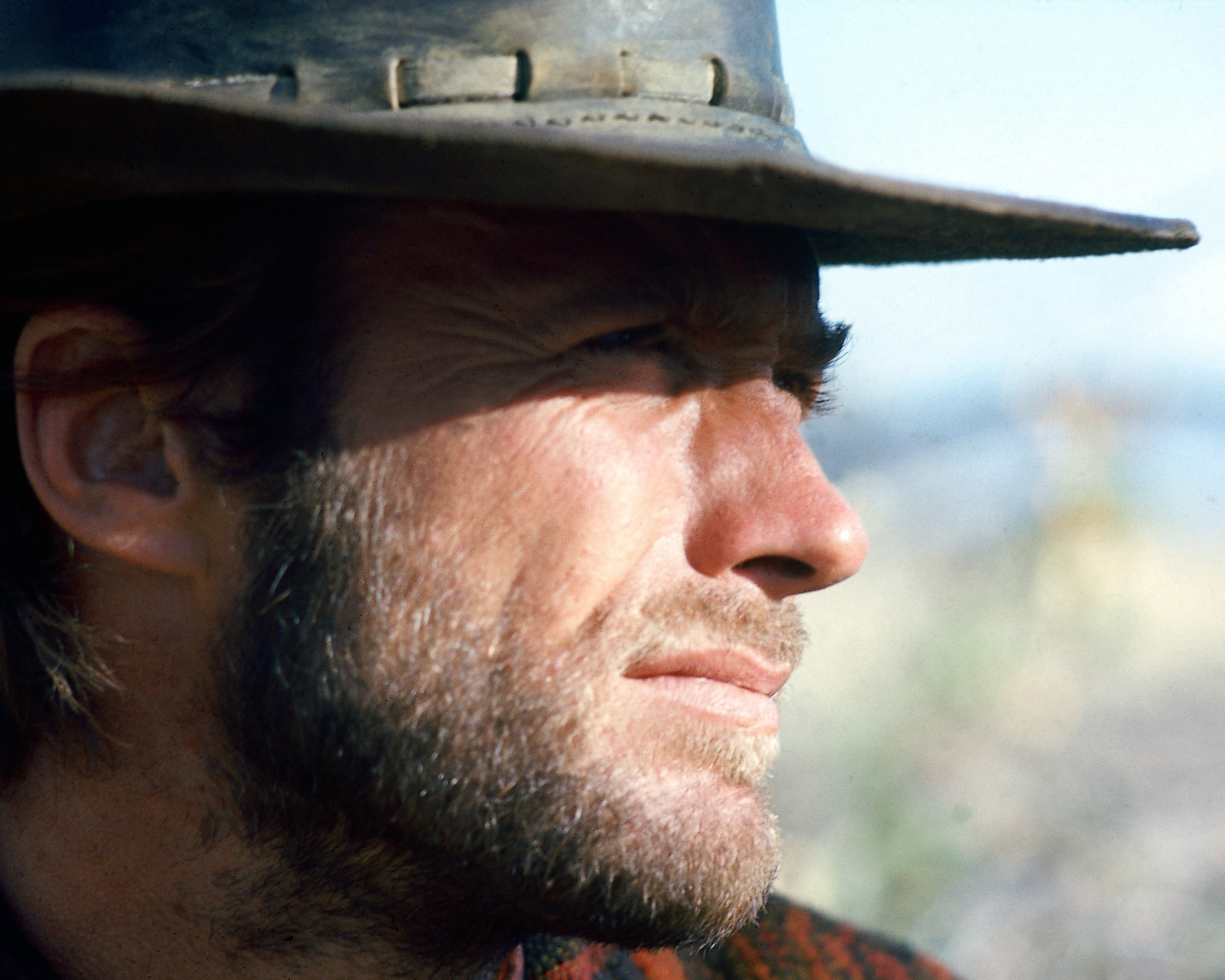 A tight profile shot from the 1970 Western "Two Mules for Sister Sara" showed Clint Eastwood wearing the weathered wide-brimmed hat associated with his character, Hogan. Sunlight cut across Clint's face as he stared into the distance, drawing attention to his narrowed eyes, prominent nose, angular jawline, and rugged stubble. The film arrived during a defining stretch of his career, when the actor had firmly established himself as one of Hollywood's most recognizable Western stars.