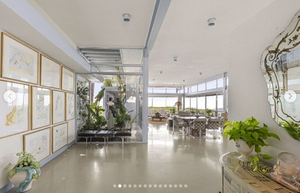 Kelly Osbourne's former Los Feliz home opens into a bright, gallery-like interior lined with framed artwork, greenery, and polished terrazzo flooring. Floor-to-ceiling windows draw the eye toward the living spaces beyond, highlighting the 1963 home's open layout and midcentury character. The image appeared in a post dated October 18, 2024. | Source: Instagram/jparkerstanton