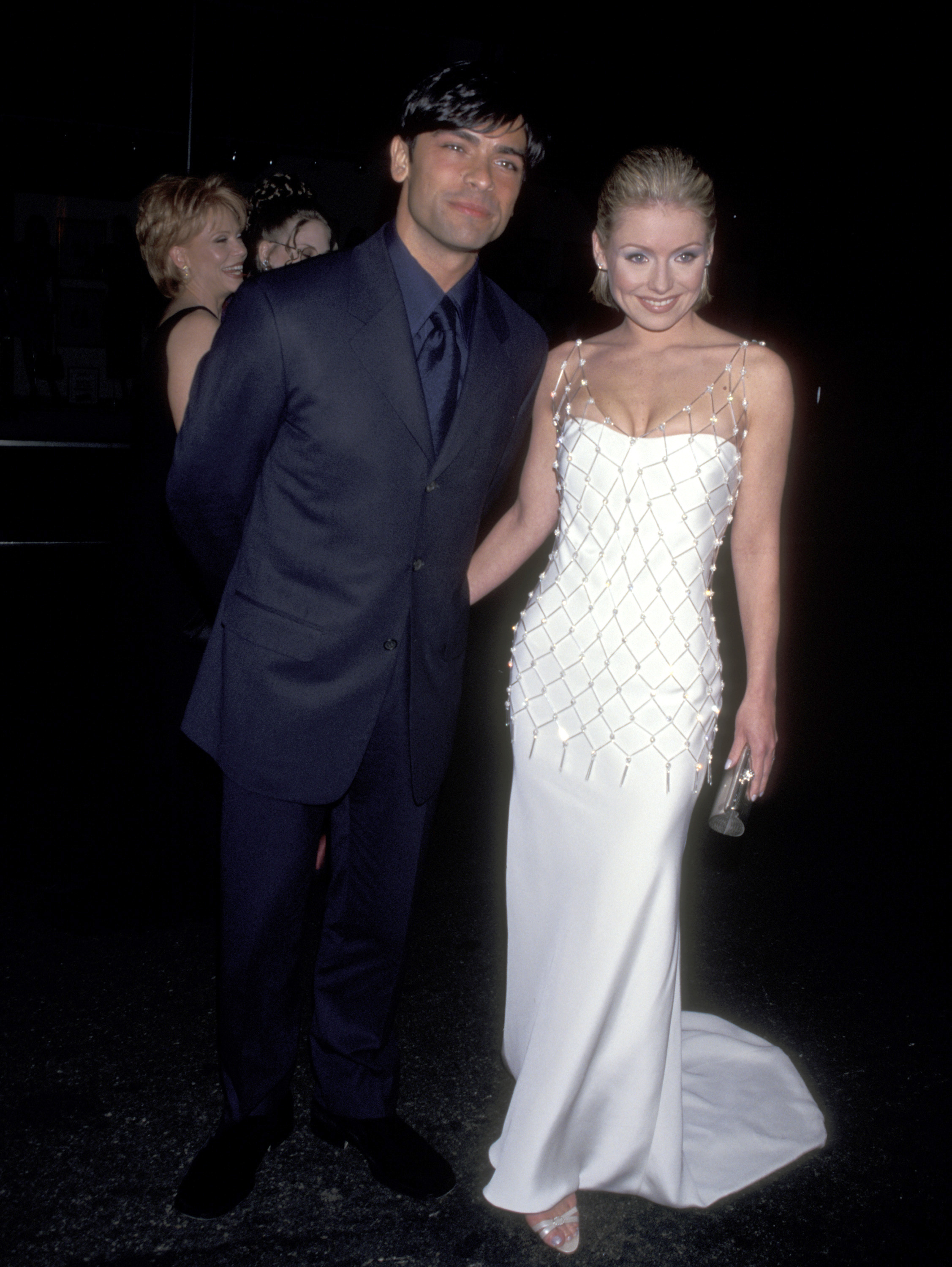 Kelly Ripa and Mark Consuelos pose together in their early years as a couple, with Kelly wearing an elegant white gown and Mark dressed in a dark suit. | Source: Getty Images.