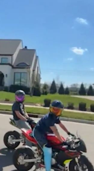 Two kids wearing helmets sit on small motorbikes at the side of the street, paused and watching the unfolding confrontation nearby. | Source: X/TMZ