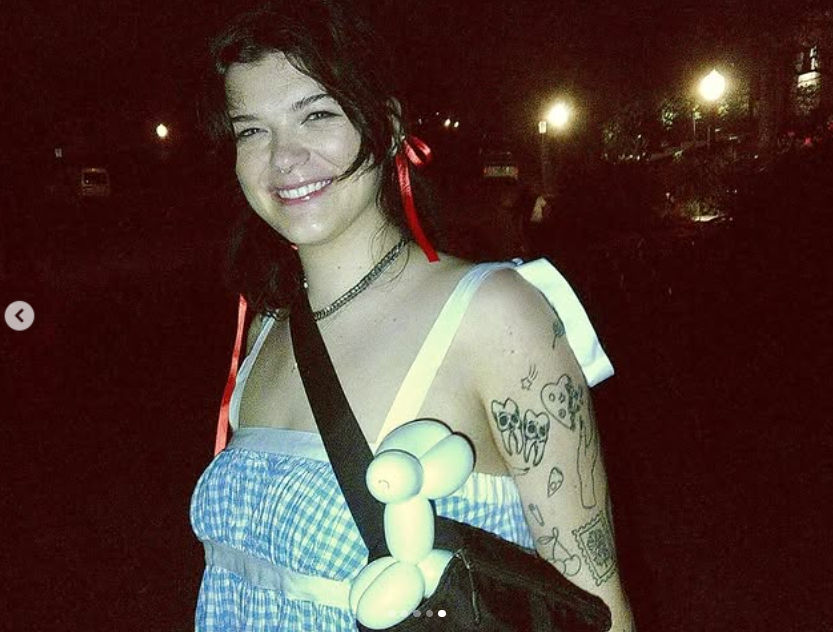 Kendall Fortner smiles, wearing a blue gingham dress with red ribbons in her hair and a playful balloon animal clipped to her bag | Source: Instagram/kendall_fortner
