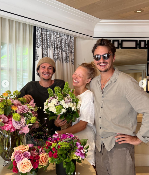 Pamela Anderson beams with joy beside her sons, Brandon Thomas Lee and Dylan Jagger Lee, completely surrounded by lavish floral arrangements. Clutching a bouquet of white roses and greenery, she shares an affectionate laugh with the boys who helped her build a peaceful life and garden on Vancouver Island. Celebrating the family bond she has always fought to protect, she captioned the Mother's Day post, "Peace, love, joy… Bless all the Mothers in the world 🤍". | Source: Instagram/pamelaanderson