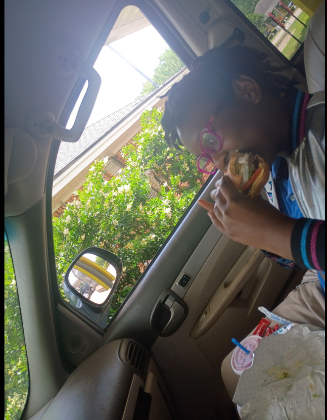 A quiet, everyday moment: seated in the passenger seat, Shamar Elkins's eldest daughter leans into a burger mid-bite, pink glasses catching the light. | Source: Facebook/Shamar Elkins