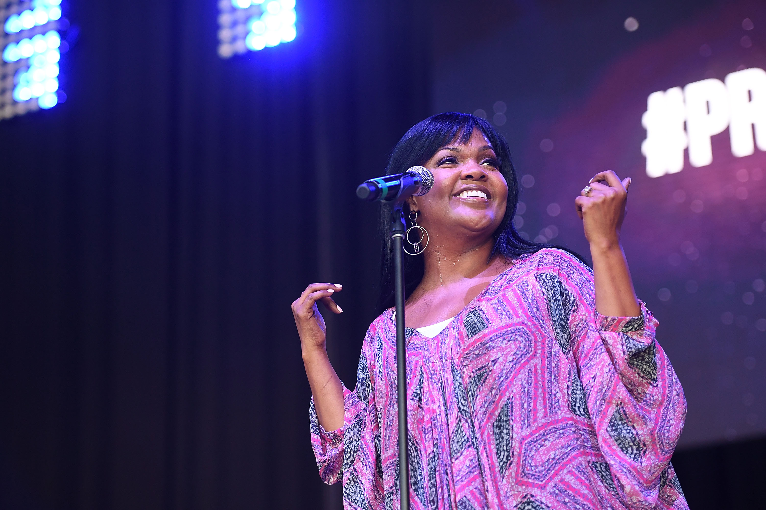 CeCe Winans smiles during her performance at Praise In The Park at Lakewood Amphitheatre in Atlanta, Georgia, on July 29, 2017, while standing beside a microphone onstage and singing.