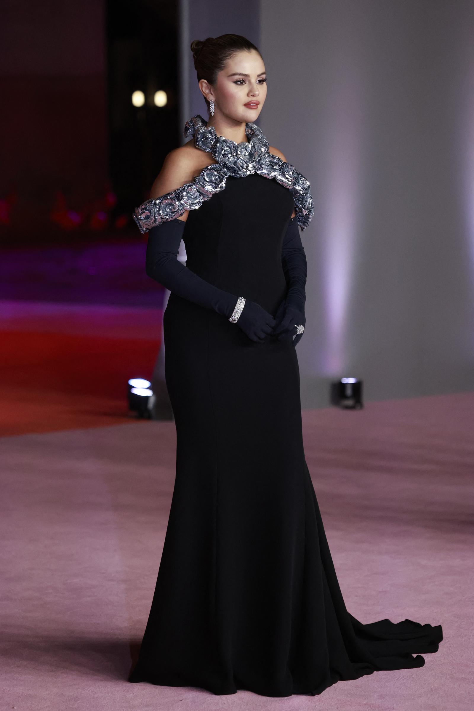 Selena Gomez poses regally in a striking black gown with silver detailing at the neckline as she attends the 3rd Annual Academy Museum Gala at the Academy Museum of Motion Pictures in Los Angeles. Adding a bold twist to her look, she pairs the dress with elegant navy blue gloves that make her stand out.