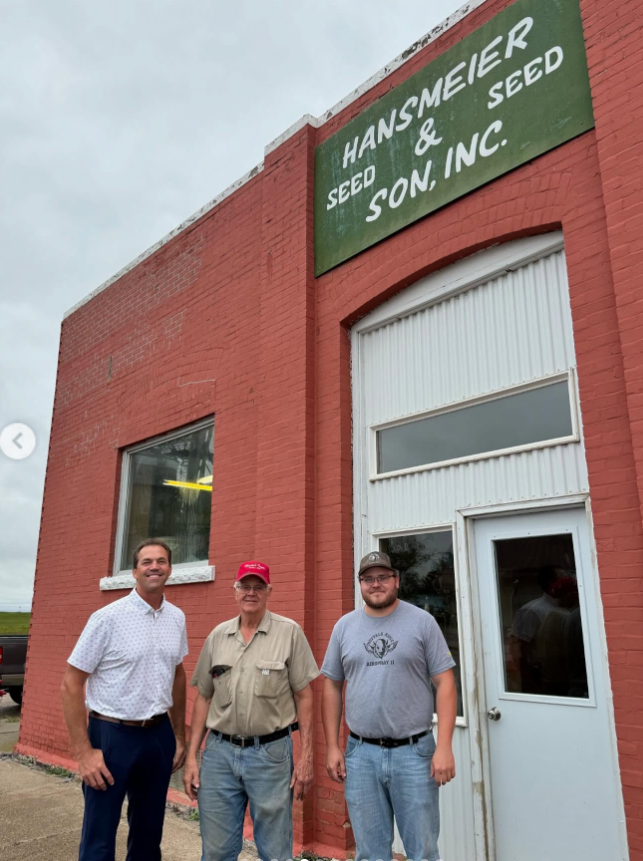 Bryon Noem stands outside Hansmeier Seed & Seed Son, Inc., smiling alongside two local men—an unpolished, small-town stop rooted in agriculture and community. | Source: Instagram/sdbryonnoem