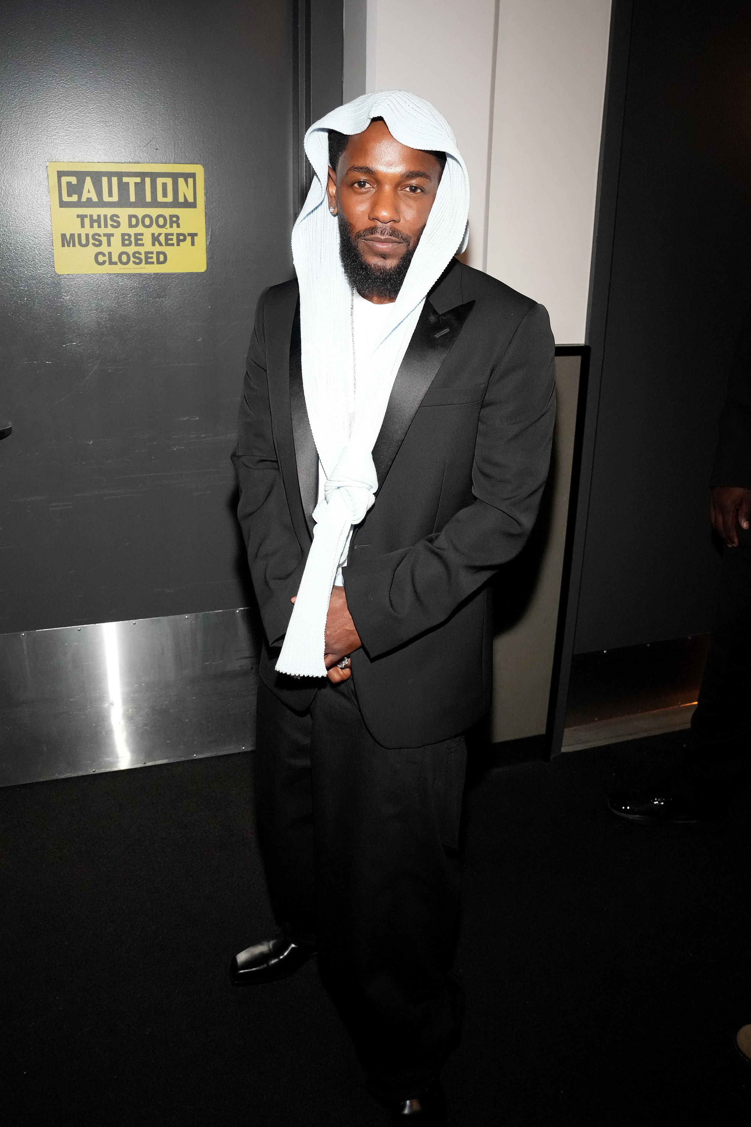 Backstage at the Peacock Theater, Kendrick Lamar poses in his full BET Awards 2025 look — a black tux paired with the now-iconic head covering, knotted in the front, which drew curiosity and commentary across social media.