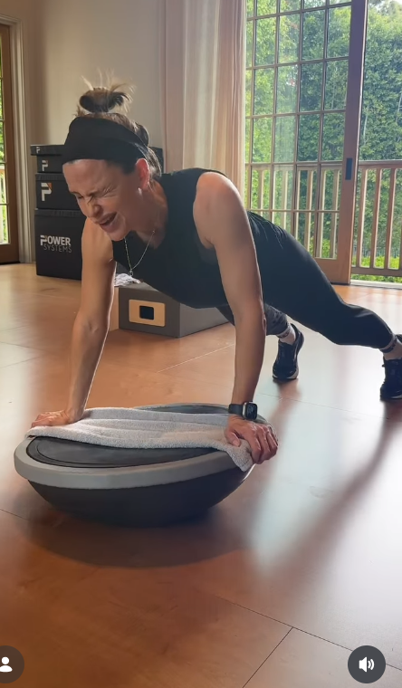 Wearing a black sleeveless top and black leggings, Jennifer Garner laughs with her eyes closed while holding the plank position in the sunlit workout space. | Source: Instagram/jennifer.garner