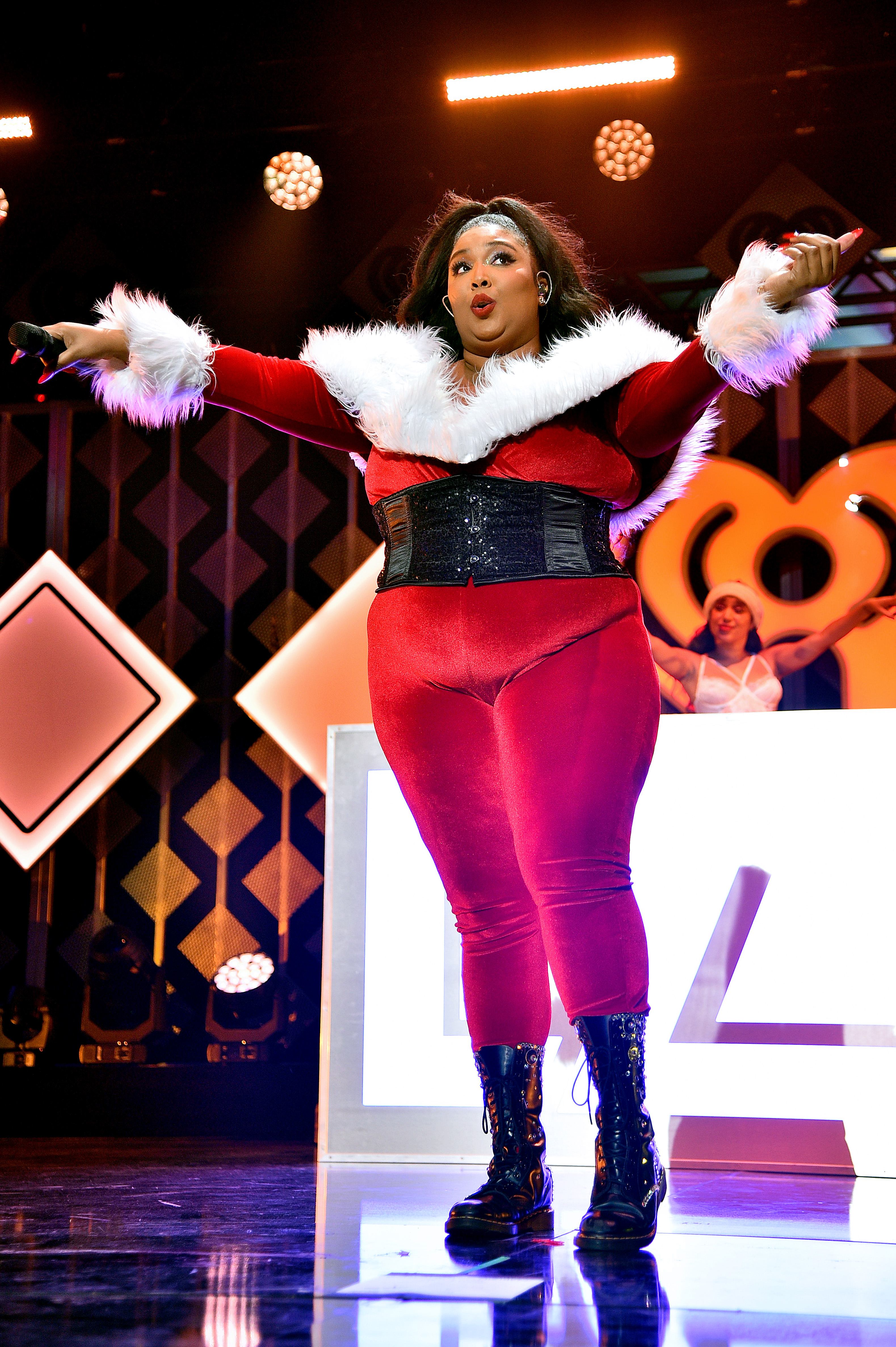 Onstage at Jingle Ball, Lizzo commands the spotlight with festive flair, her arms outstretched as she connects effortlessly with a massive audience. In a bold, high-energy look, the moment captures her dominance — where hitmaker status meets undeniable stage presence.