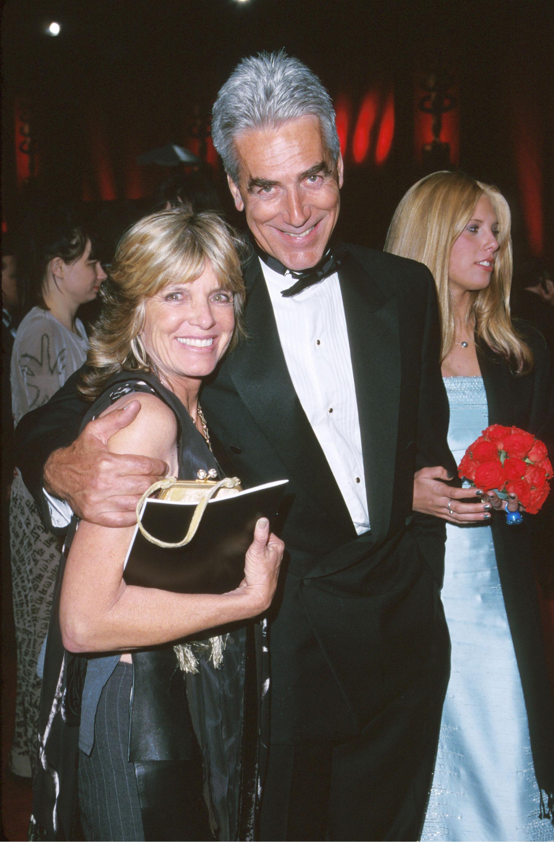 Stepping out for cinema's biggest night, Sam Elliott and Katharine Ross attended the 72nd Annual Academy Awards on March 26, 2000, at the Shrine Auditorium in Los Angeles, California. Sam embraced his wife in a classic black tuxedo with a bowtie, sporting a rare clean-shaven look without his trademark mustache, while Katharine smiled radiantly in an elegant black ensemble complemented by their daughter, Cleo Rose Elliott, posing nearby in an icy-blue gown. | Source: Getty Images