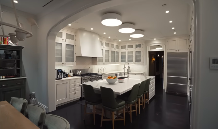 The white kitchen is sleek but not severe, with a large island that anchors the room. Its brightness offers a calm counterpoint to the home's darker, more theatrical corners. | Source: YouTube/Architectural Digest