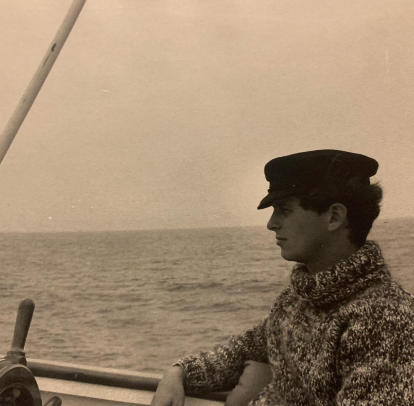 A vintage photograph shows Stephen Wyle, Noah Wyle’s father, wearing a sailor-style cap and a thick knitted sweater while sitting aboard a boat with the sea stretching behind him. | Source: Instagram/therealnoahwyle