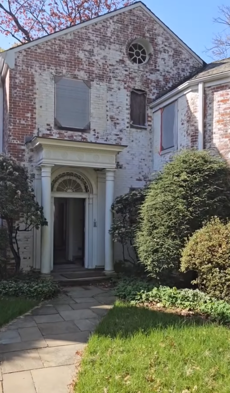 The front entrance of Richard Gere's former Connecticut estate featured a weathered brick facade, a columned portico, and mature landscaping surrounding a stone walkway. | Source: Instagram/hudsonvalleyhouseparts