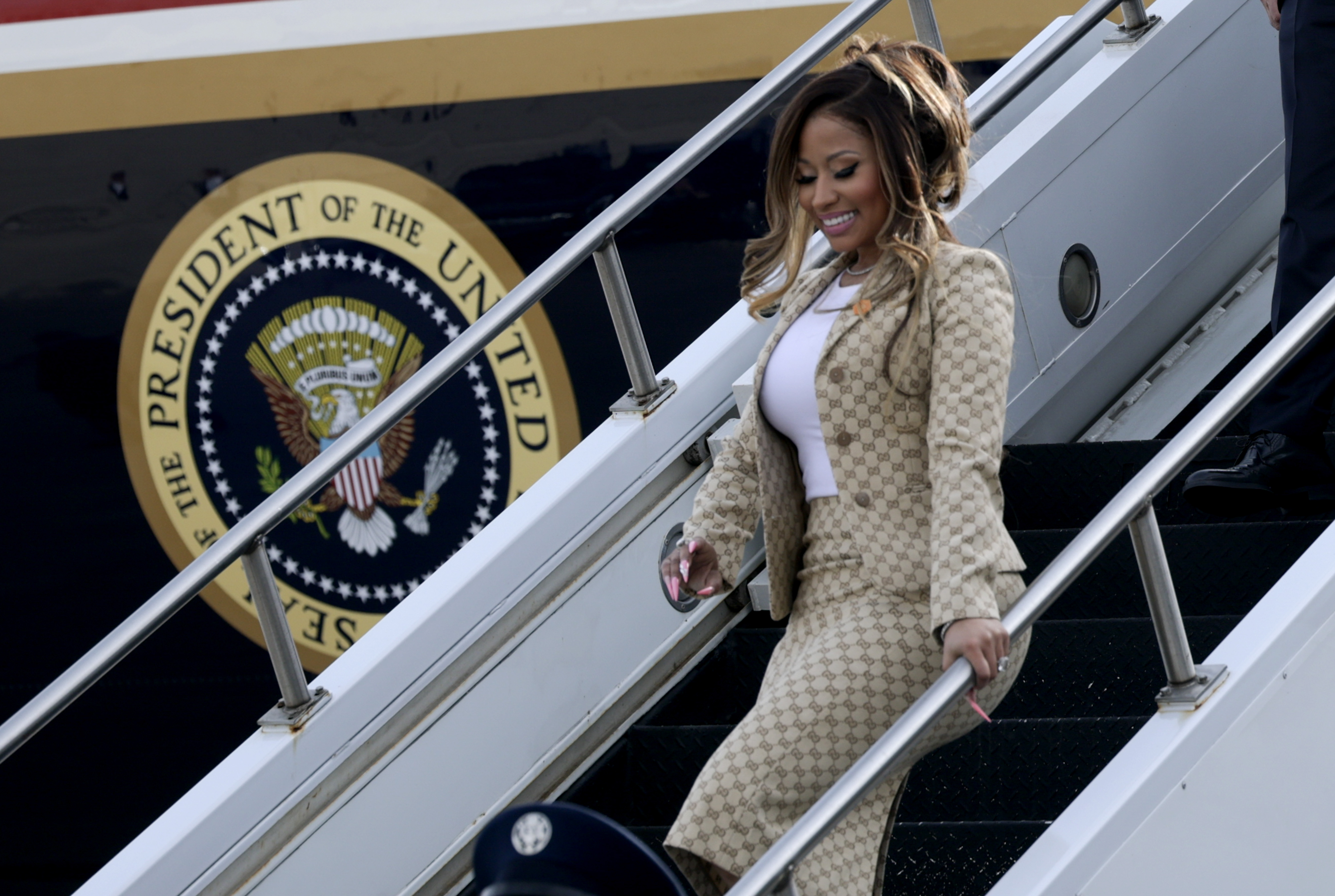 Nicki Minaj smiles as she descends the aircraft stairs, with the official presidential seal prominently displayed behind her — an unusual arrival for a rapper whose public appearances are more often associated with concert stages and red carpets. | Source: Getty Images