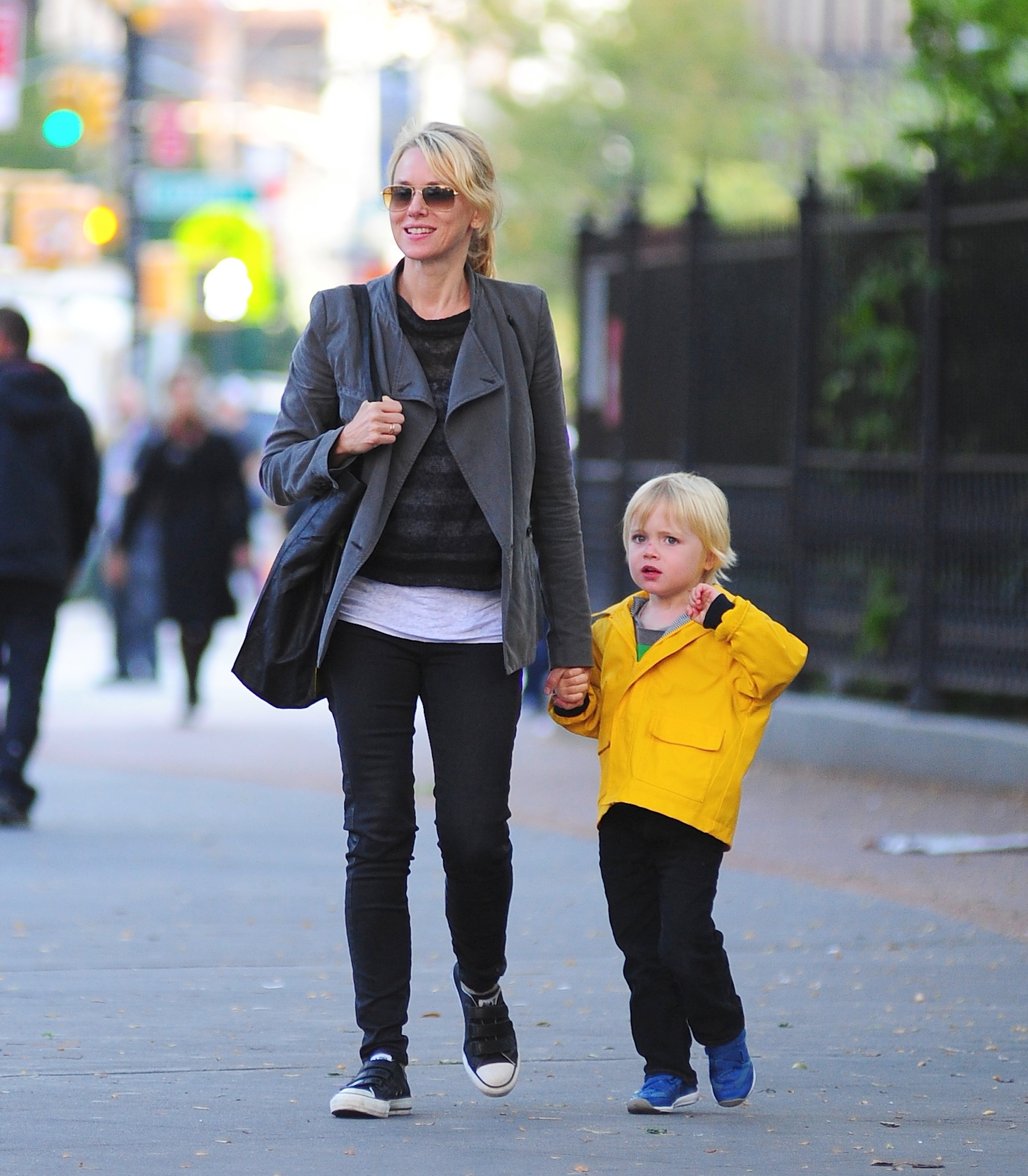 A young Kai Schreiber walked hand in hand with mother Naomi Watts along a Tribeca sidewalk on October 10, 2012, in New York City. Sporting a bright yellow zip-up jacket, black pants, and blue sneakers, the blond toddler stayed close to Watts, who smiled behind tinted sunglasses in an open charcoal blazer, layered casual tops, skinny trousers, and black low-top sneakers. | Source: Getty Images