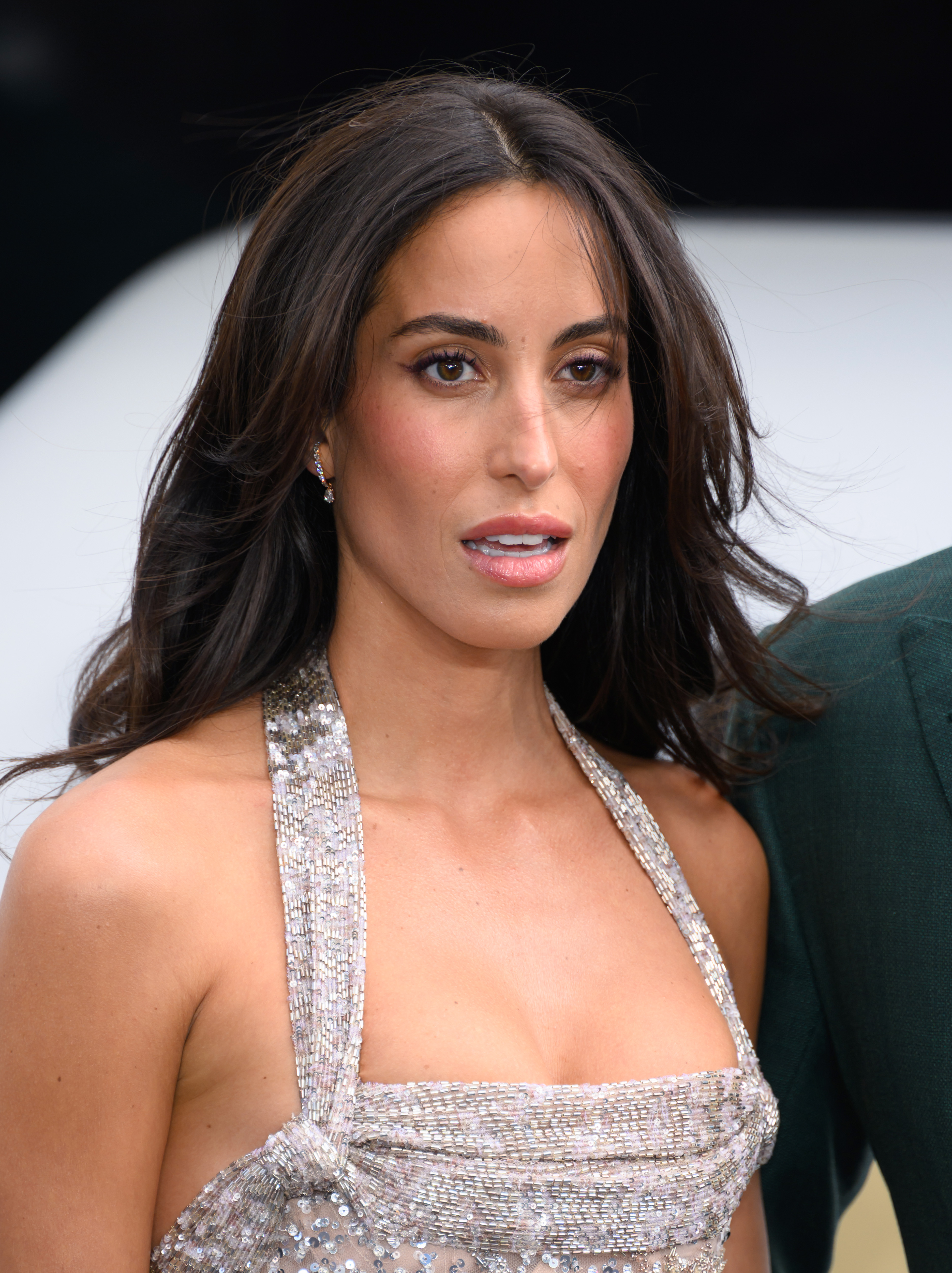 Ines de Ramon poses in a shimmering silver gown at the London premiere of "F1: The Movie," with soft curls framing her face as she looks toward photographers on the red carpet.
