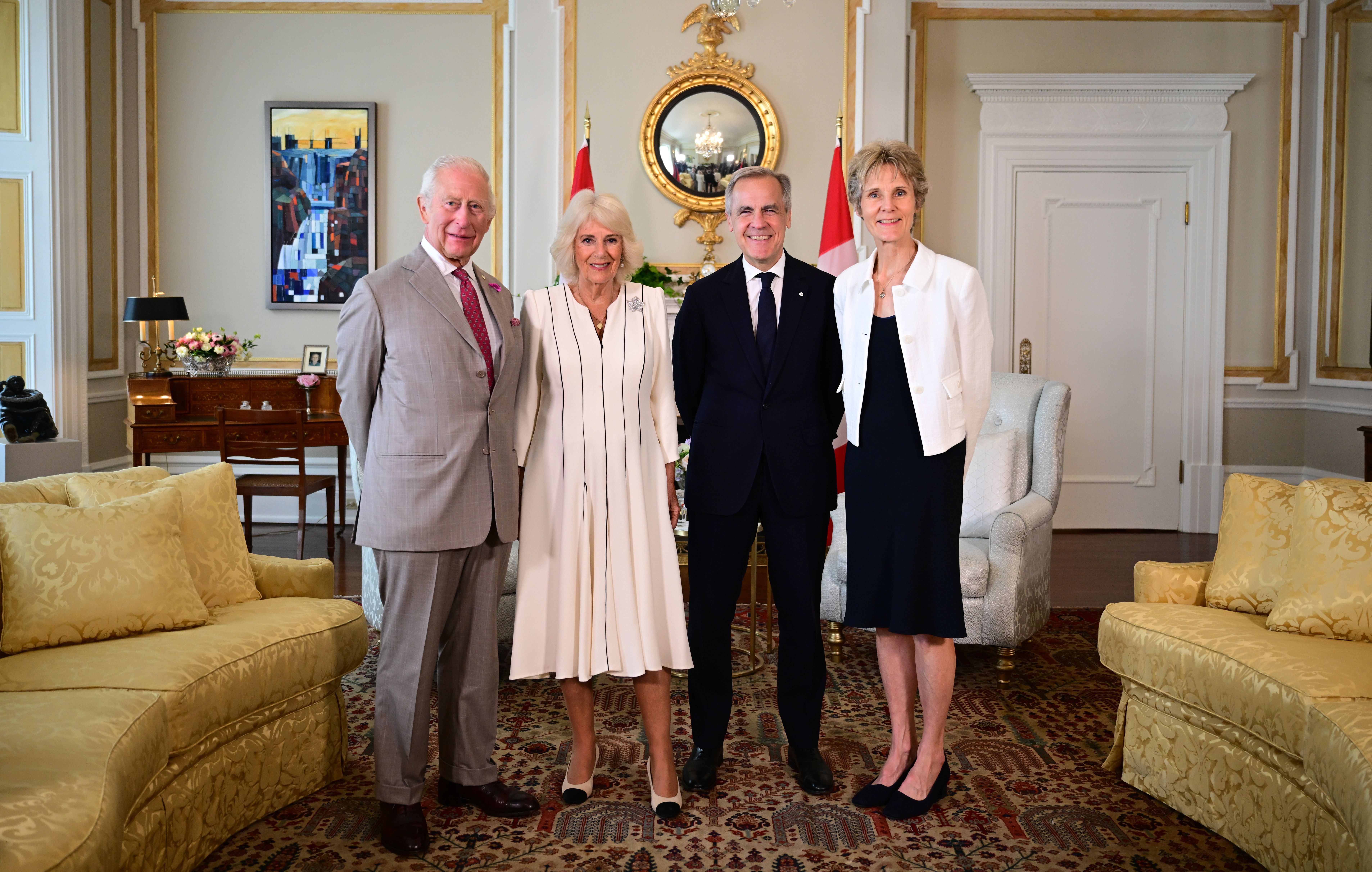 Later, indoors at Rideau Hall, King Charles III and Queen Camilla pose for a beautiful official picture with Prime Minister Mark Carney and his wife Diana Fox Carney, capturing a moment of formal elegance.