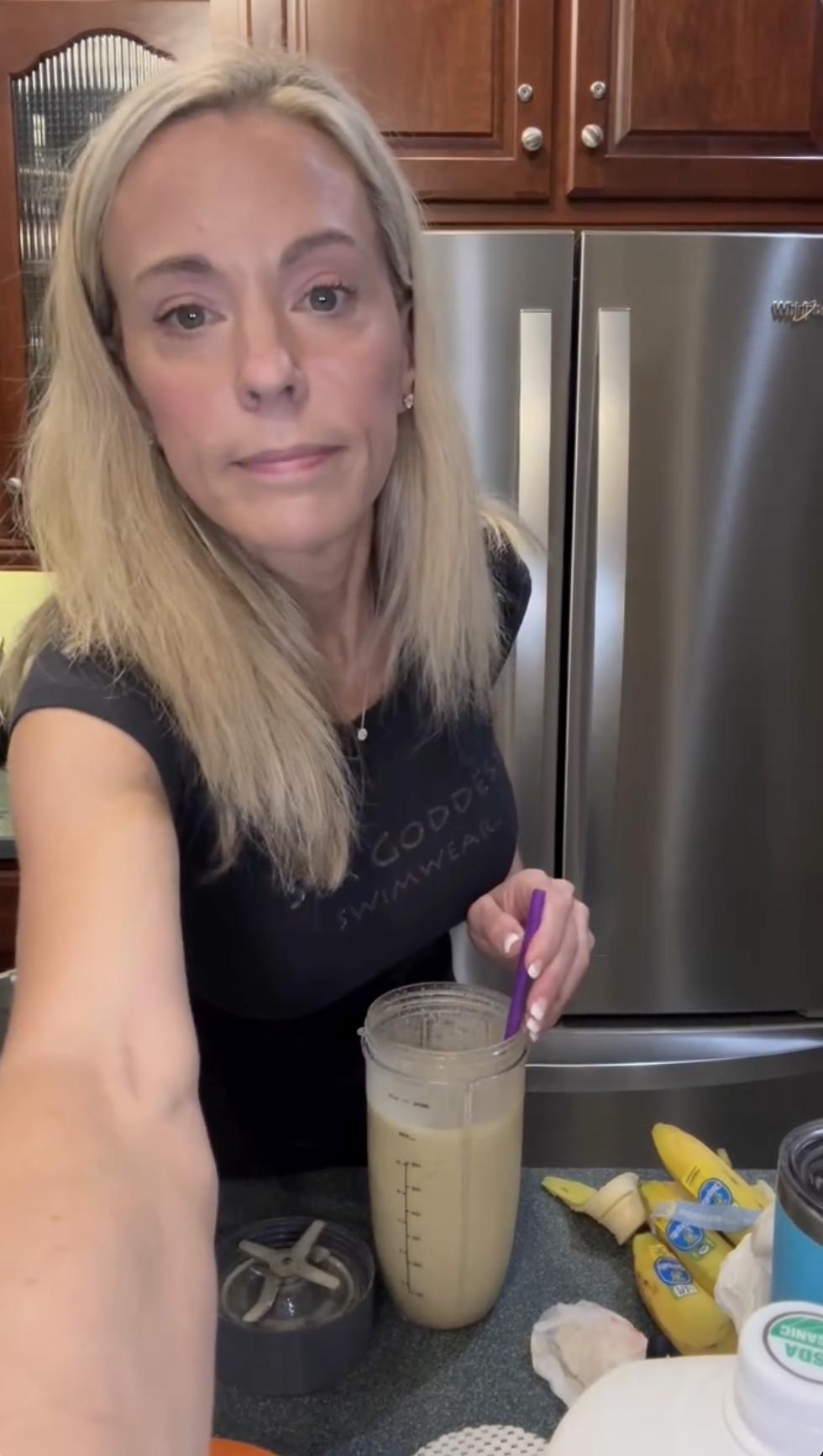 Holding a spoon in one hand and a blender cup in the other, Kate Gosselin leans toward the camera. With her drink mixed and bananas scattered on the counter, she looks straight ahead, sharing a candid kitchen moment. | Source: Instagram/kateplusmy8