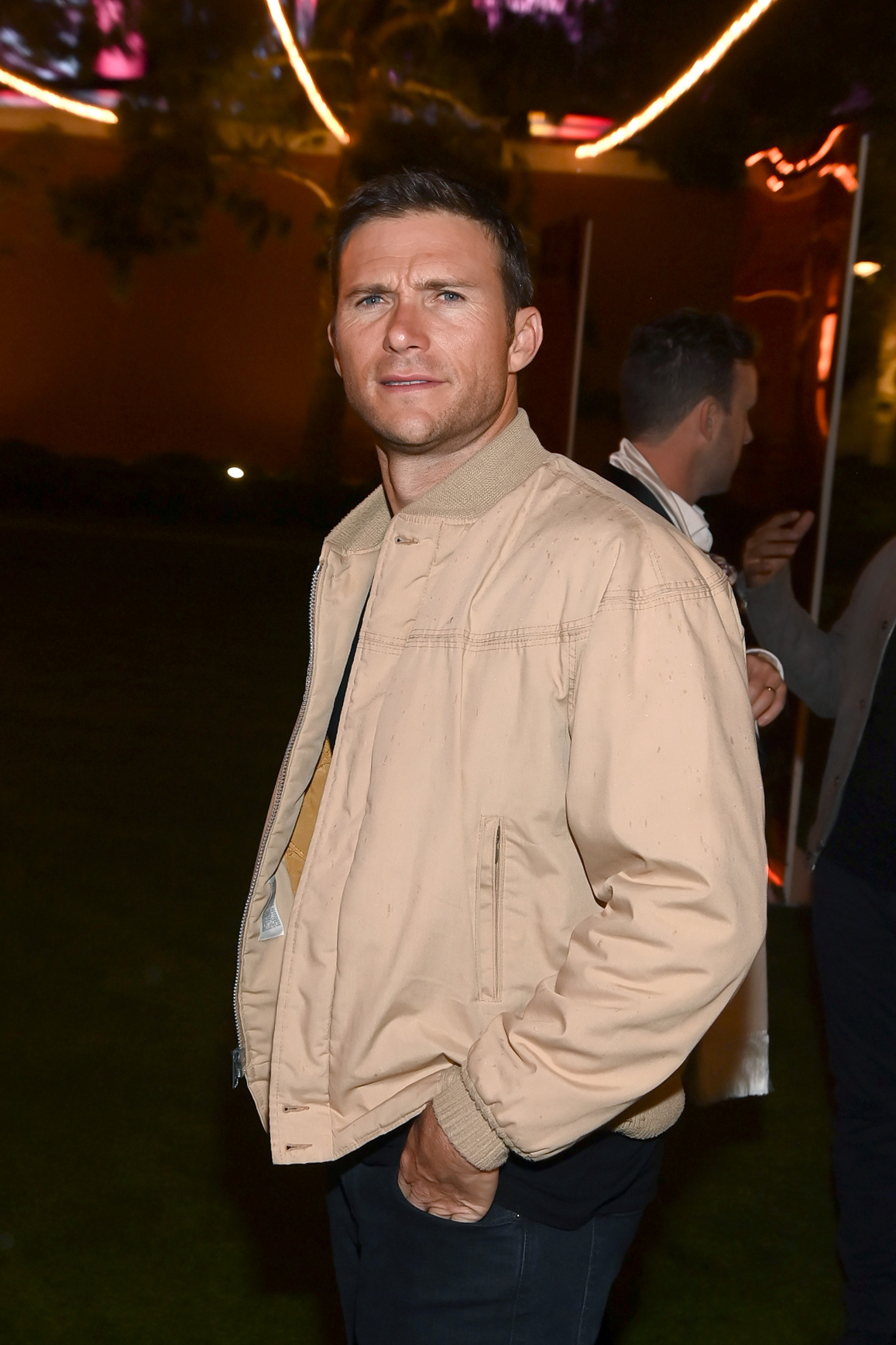 Scott Eastwood attended amfAR Las Vegas 2025 at Wynn Las Vegas in Nevada on November 21, 2025, stepping out in a beige jacket and dark pants for the evening event. Photographed beneath the venue's warm lights with one hand tucked casually into his pocket, Scott wore his short hair neatly styled as his blue eyes, strong jawline, and furrowed brow stood out. The candid shot offered another angle on the facial features behind the comparisons to his famous father.