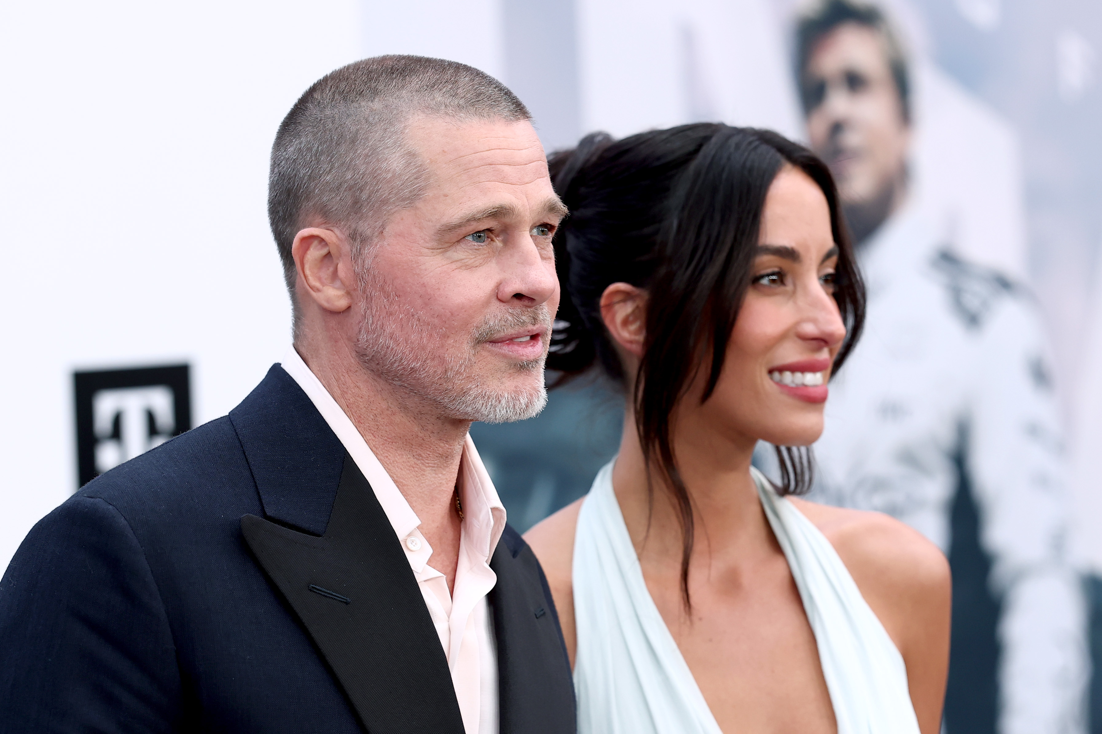 Brad Pitt and Ines de Ramon stand side-by-side during the "F1" world premiere in New York, with Pitt in a dark suit and de Ramon smiling beside him in a halter gown.