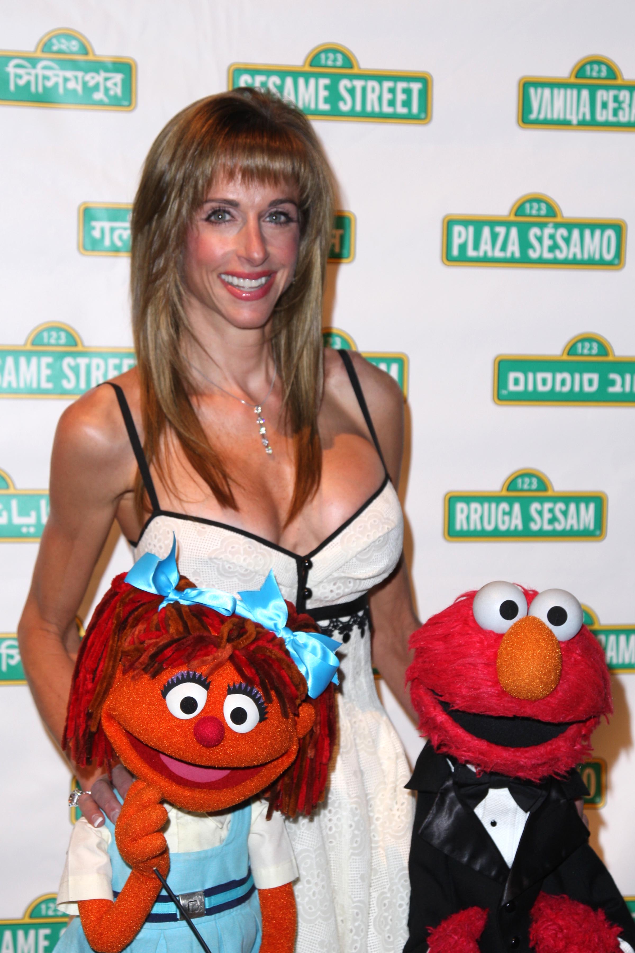 Susan Dell poses with Chamki and Elmo at the Anderson Cooper and Elmo-hosted sixth annual Sesame Workshop Benefit Gala at Cipriani’s 42nd St. in New York City. Her long hair and bangs framed a polished look as she joined the colorful Sesame Street characters.