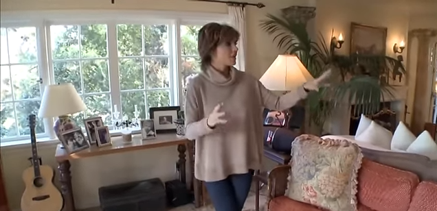 Framed family photos sit atop a rustic wooden console table right behind a warm-hued patterned sofa. | Source: YouTube/@Biography
