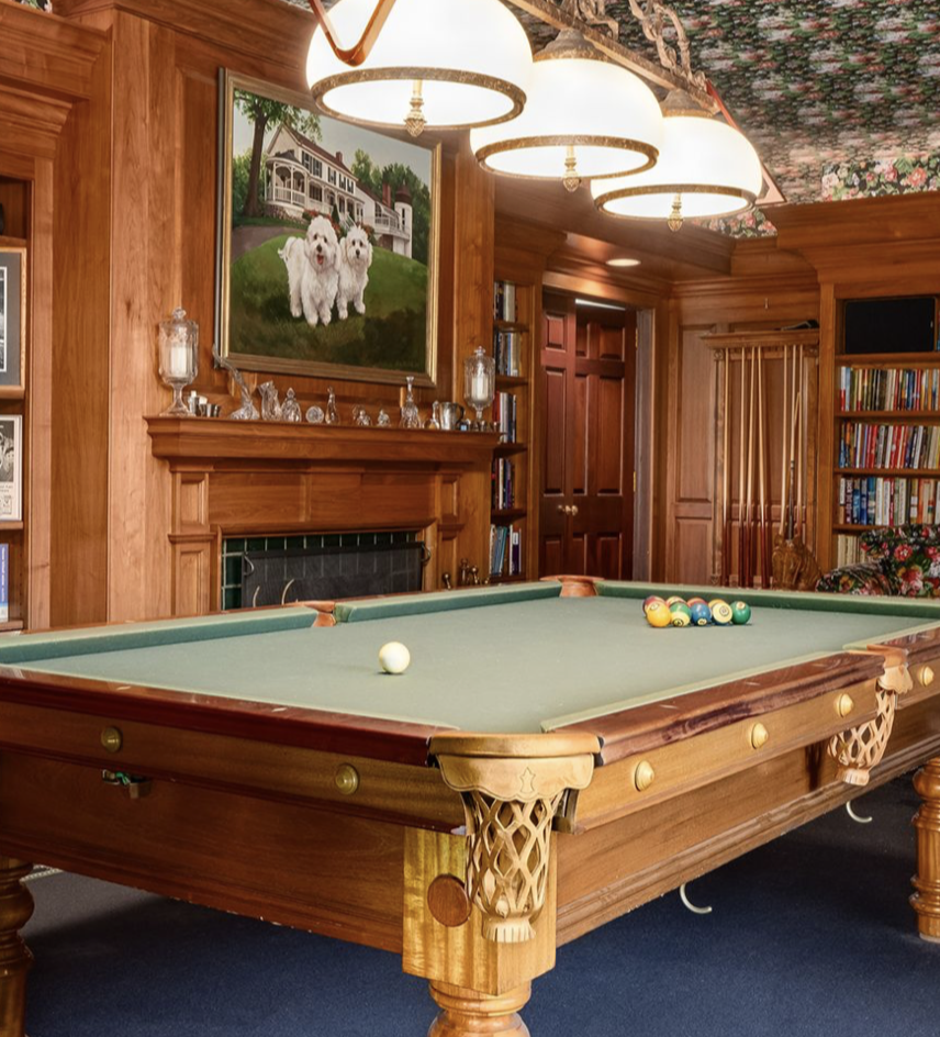 Cedar Cliff's billiards room features rich wood-paneled walls, a fireplace, and a painting of two dogs above the mantel — a personal touch that gives the luxurious space a warm, family-home atmosphere. | Source: Instagram/@robbreport