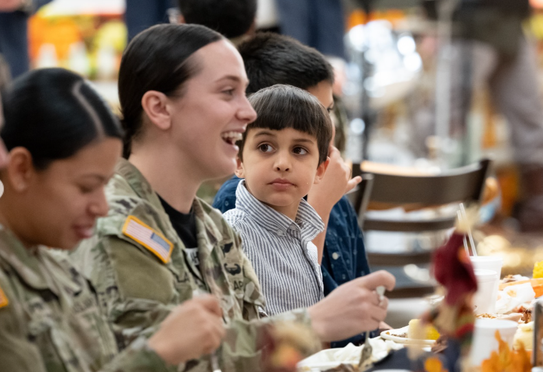 One of the JD Vances's children sits at a table eating alongside service members in uniform, looking up as others around him smile and converse during the meal. | Source: Instagram/vp