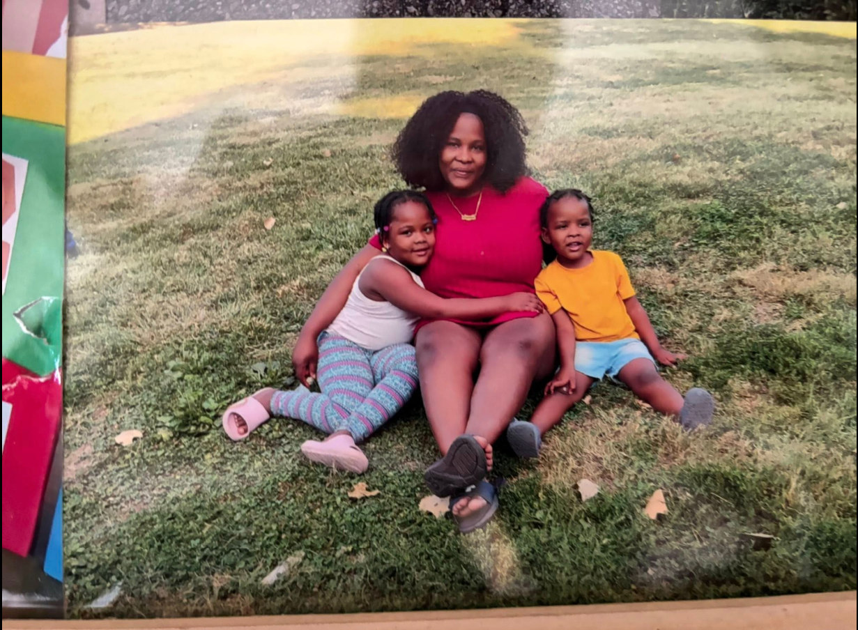 Tadens Joseph sits beside a woman and another child as the family poses together on the grass for an outdoor photo. | Source: Facebook/Eric Graves