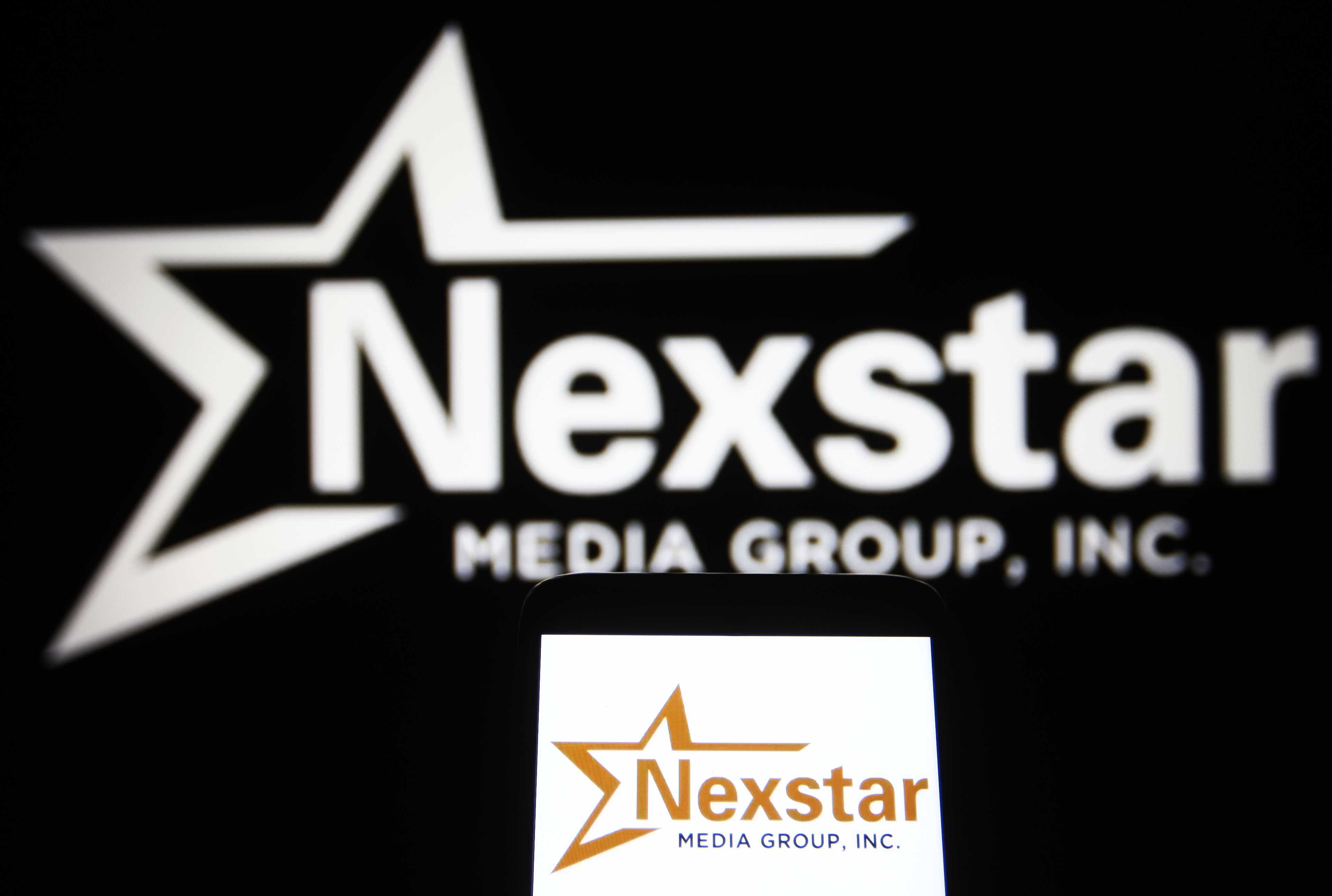 A photo of Nexstar Media Group, Inc. logo is seen on a smartphone and a pc screen | Source: Getty Images