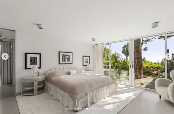 Inside the primary bedroom, a muted palette keeps attention on the surrounding landscape, visible through large sliding glass doors. The spacious room features a low bed, minimal furnishings, and direct terrace access, allowing sunlight and greenery to become prominent elements of the otherwise restrained retreat. | Source: Instagram/jparkerstanton