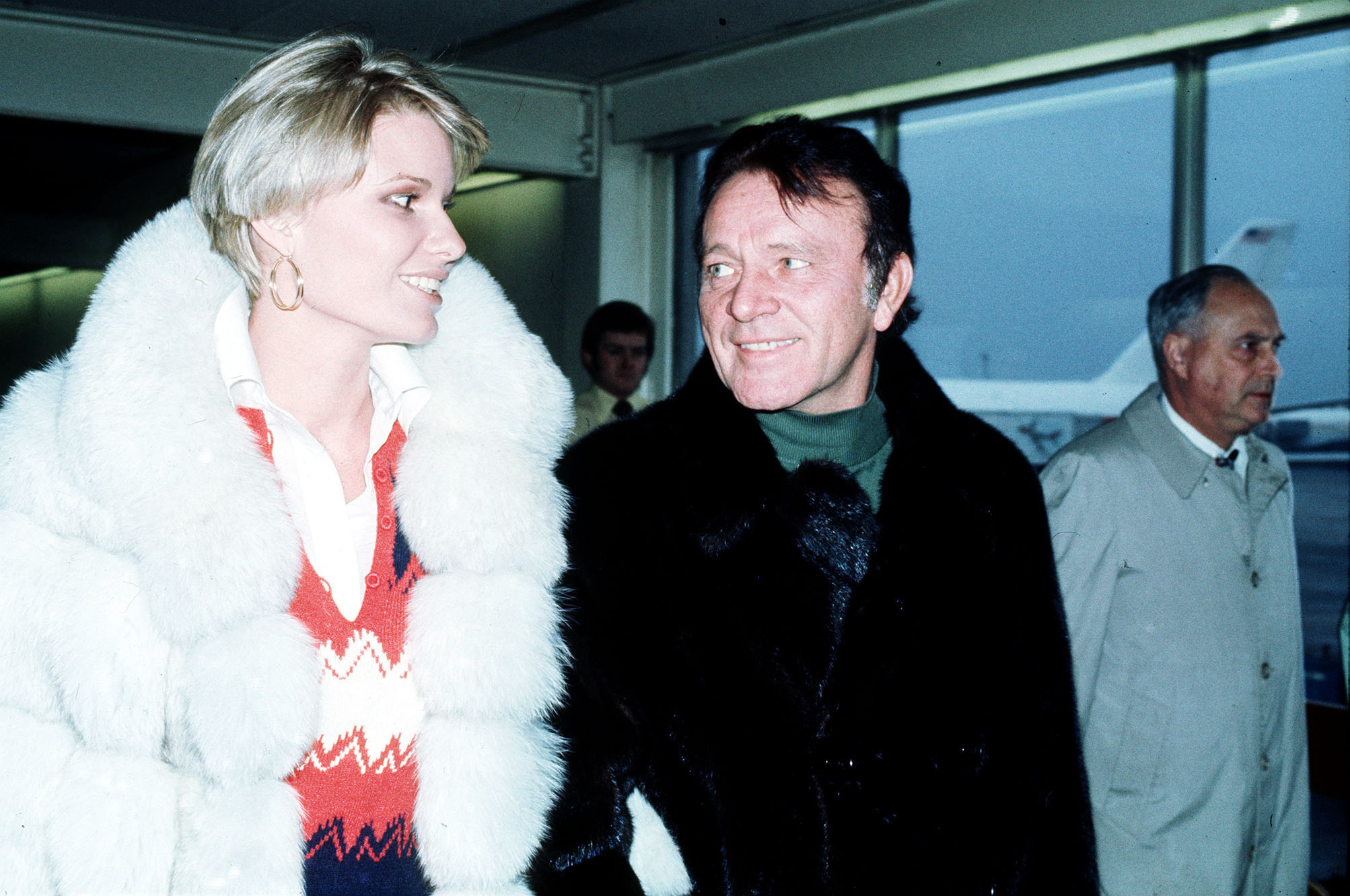 Suzy Miller and Richard Burton at Heathrow Airport in London, England, on December 12, 1976. | Source: Getty Images