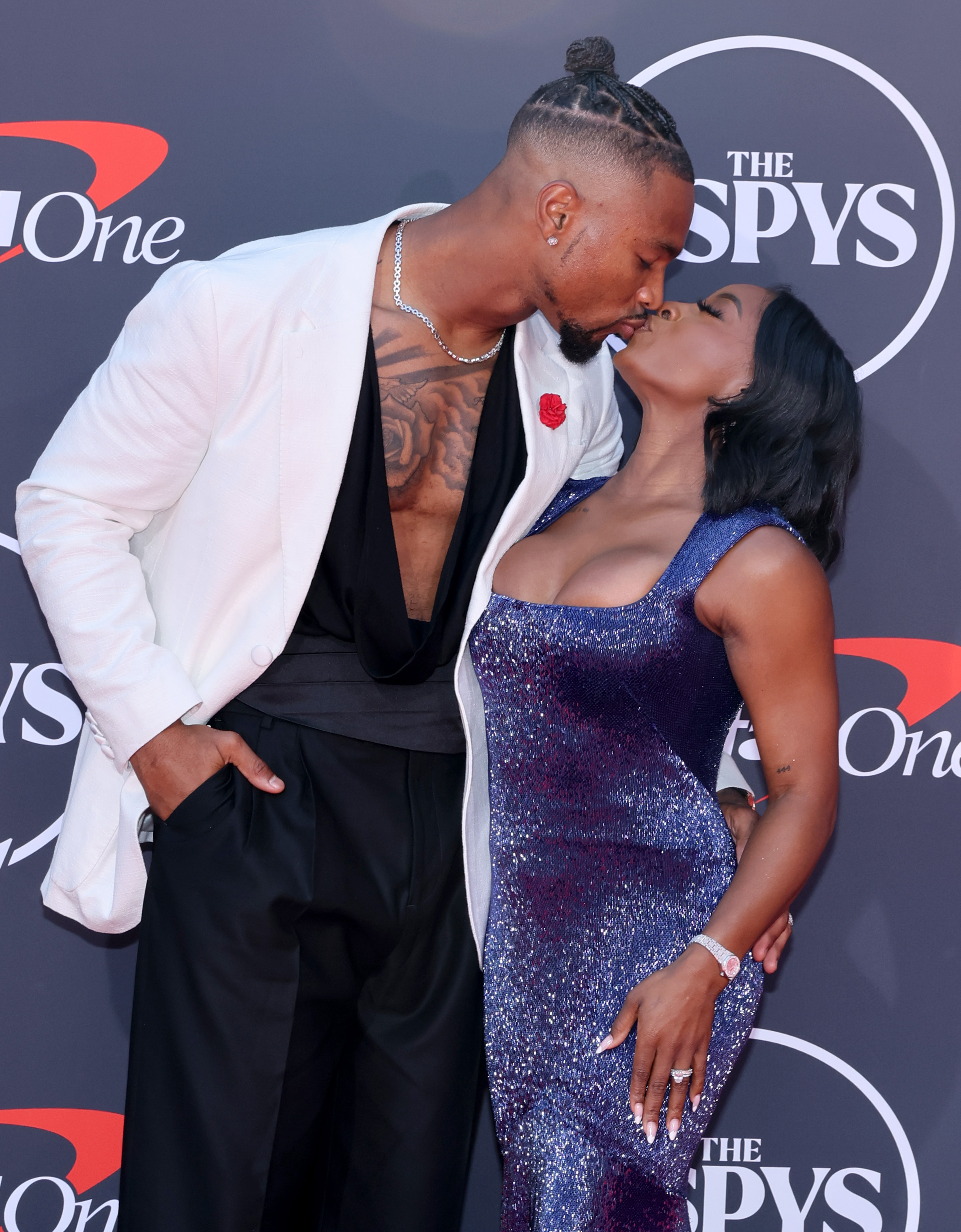 Simone Biles and Jonathan Owens share a kiss on the red carpet, pausing for a tender moment in front of photographers. With their arms wrapped around each other, the couple leans in for the affectionate gesture, highlighting their close bond during the high-profile appearance.